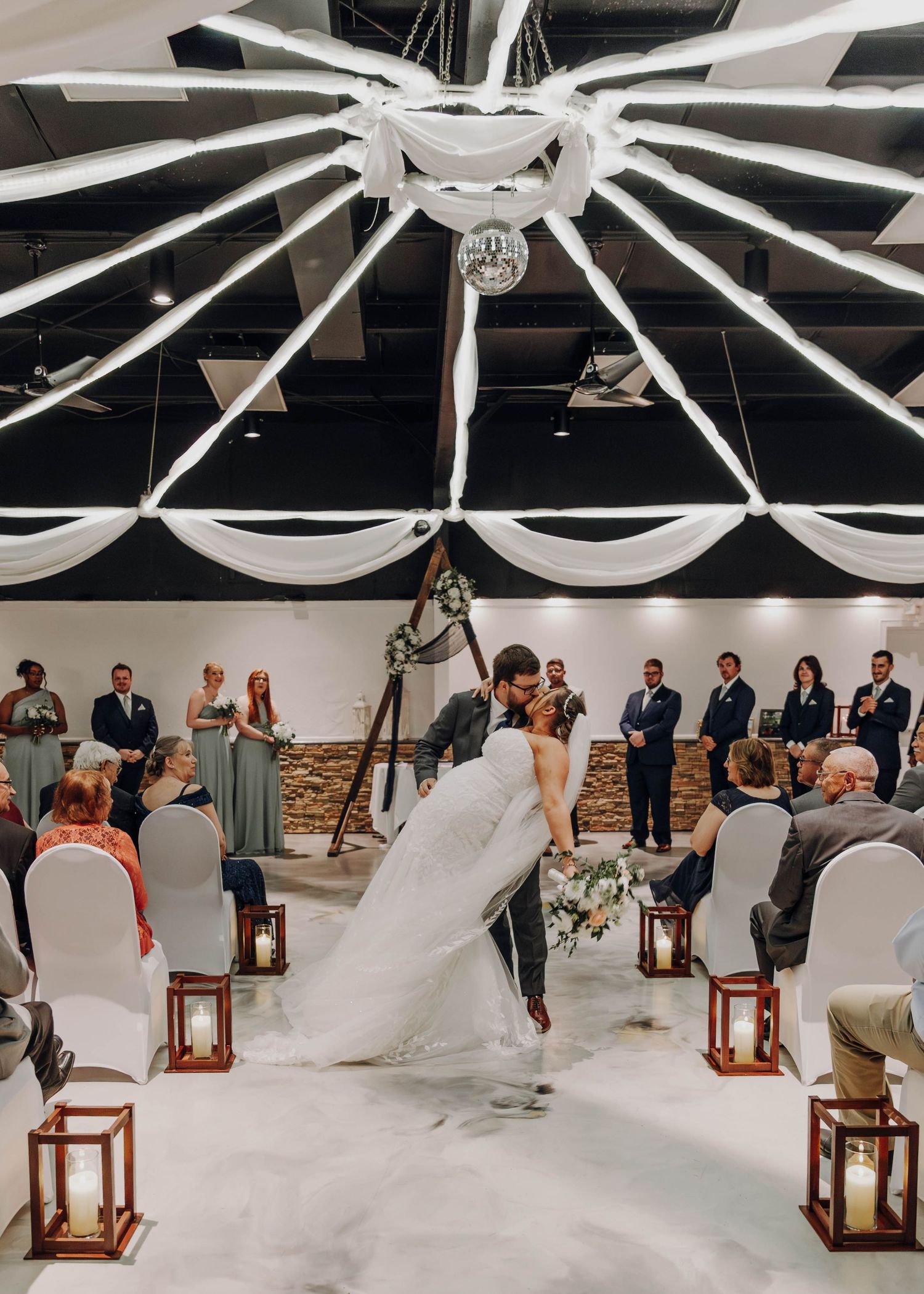 Indoor wedding ceremony setup with white ceiling draping and lantern decorations.