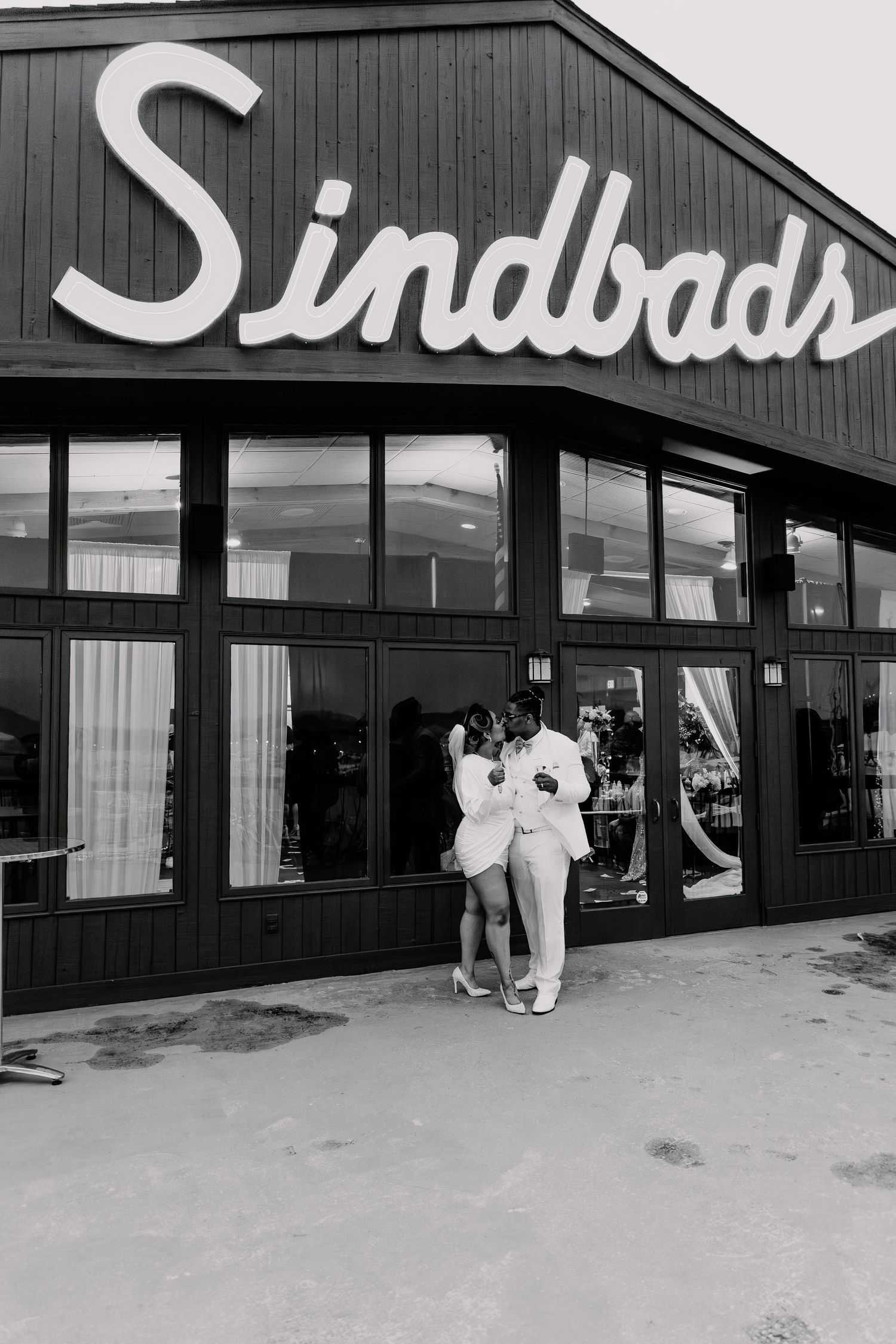 Couple poses in white attire outside Sindbads restaurant building.