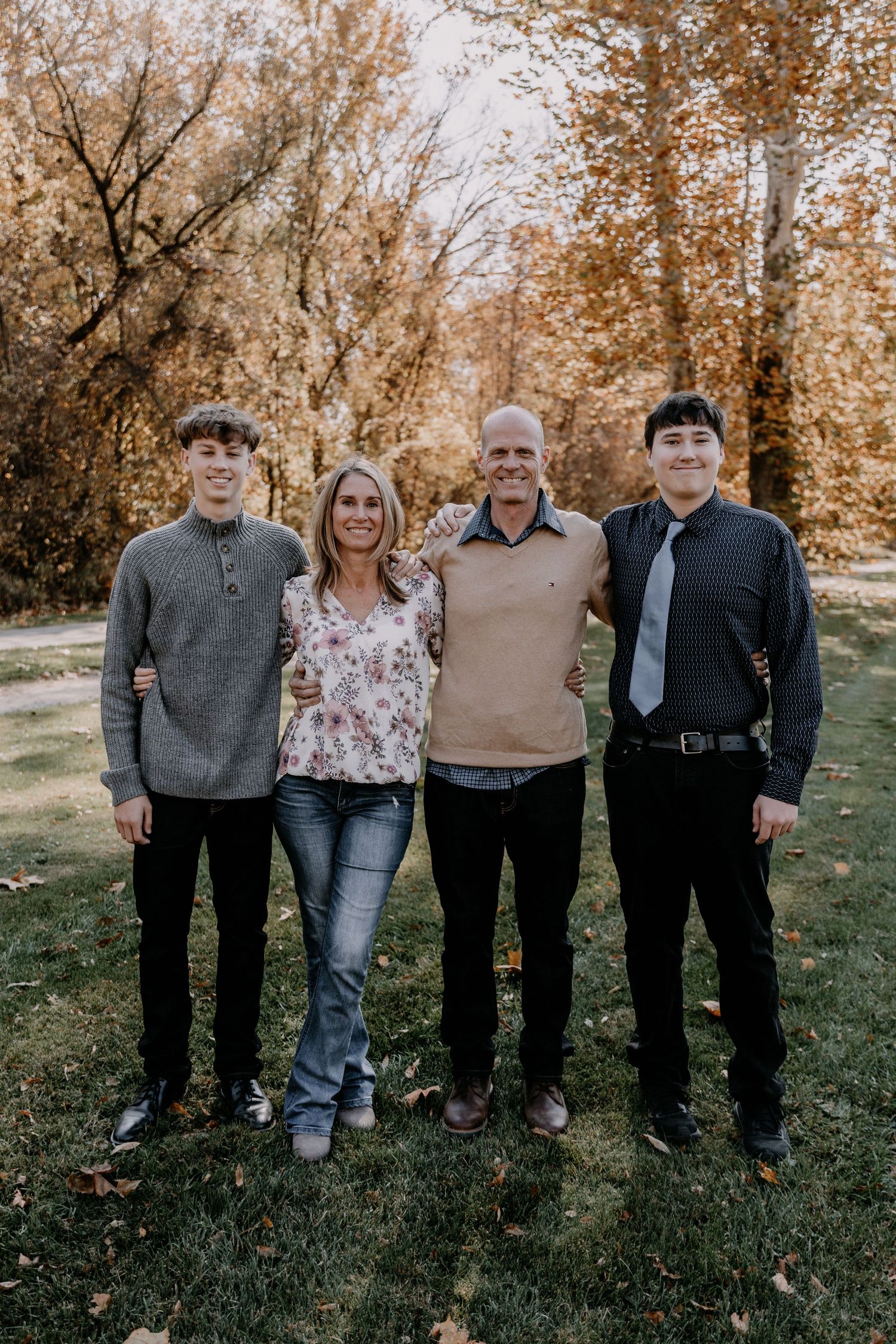 Family of four posing together on grass with fall foliage in background.