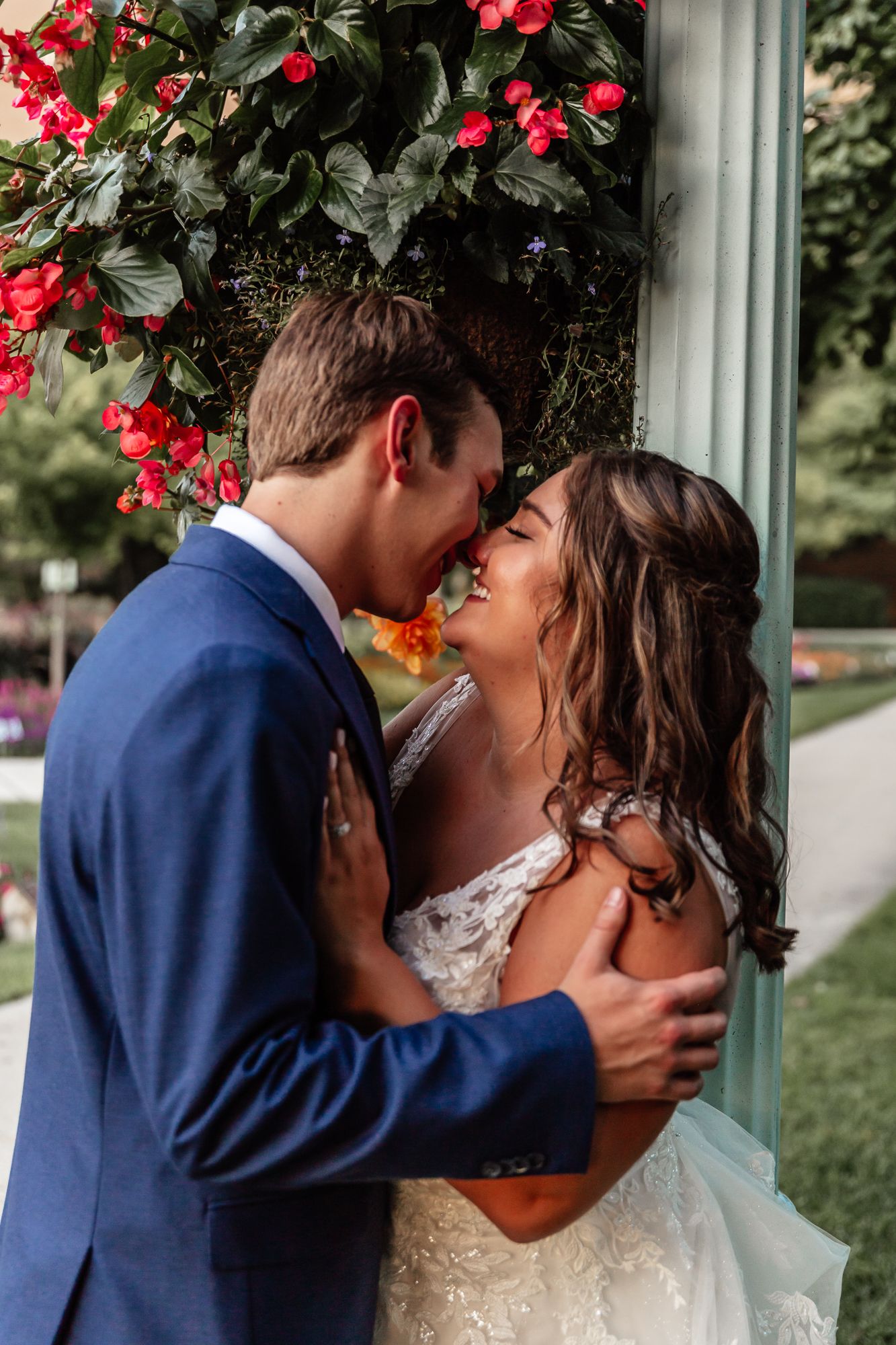 Romantic wedding couple sharing an intimate moment under red flowering vines.