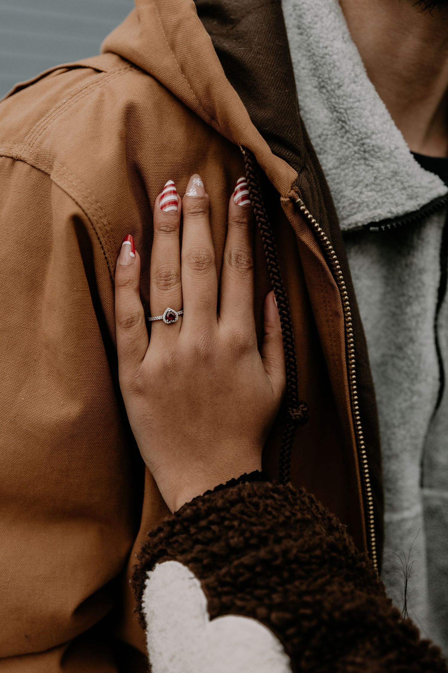 Close-up shot of an engagement ring on a hand resting against a brown jacket with sherpa lining.
