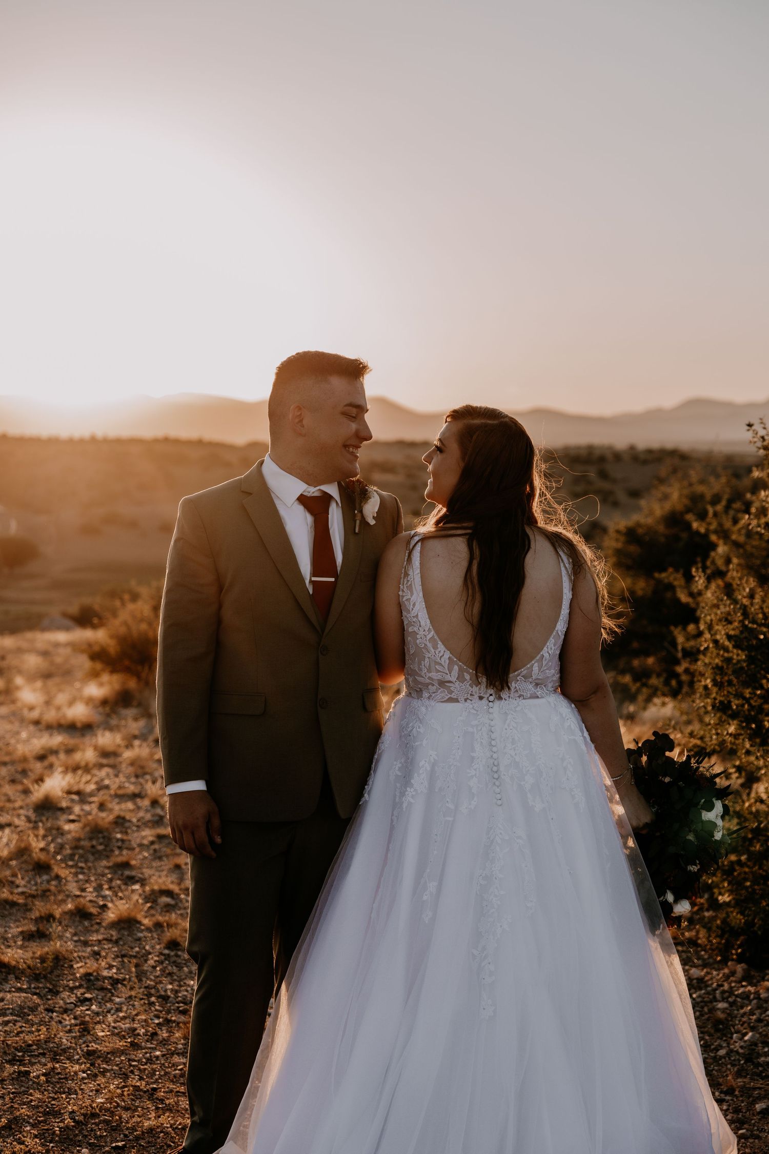 Bride in lace ballgown and groom share intimate moment during desert sunset photoshoot.