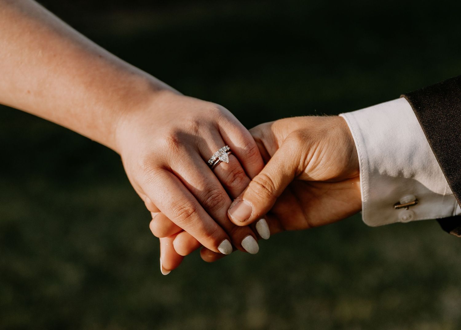 Wedding rings and held hands showcasing elegant manicure and jewelry.
