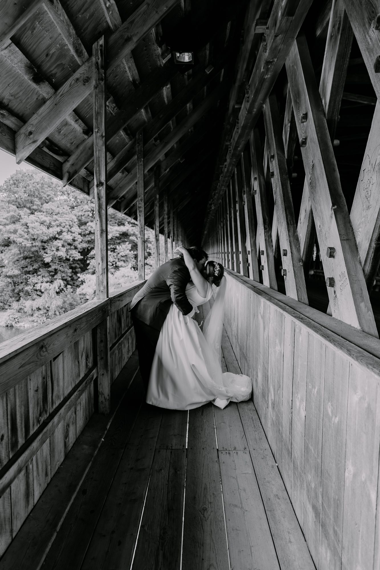 Black and white photo of bride in covered bridge corridor creating dramatic perspective.