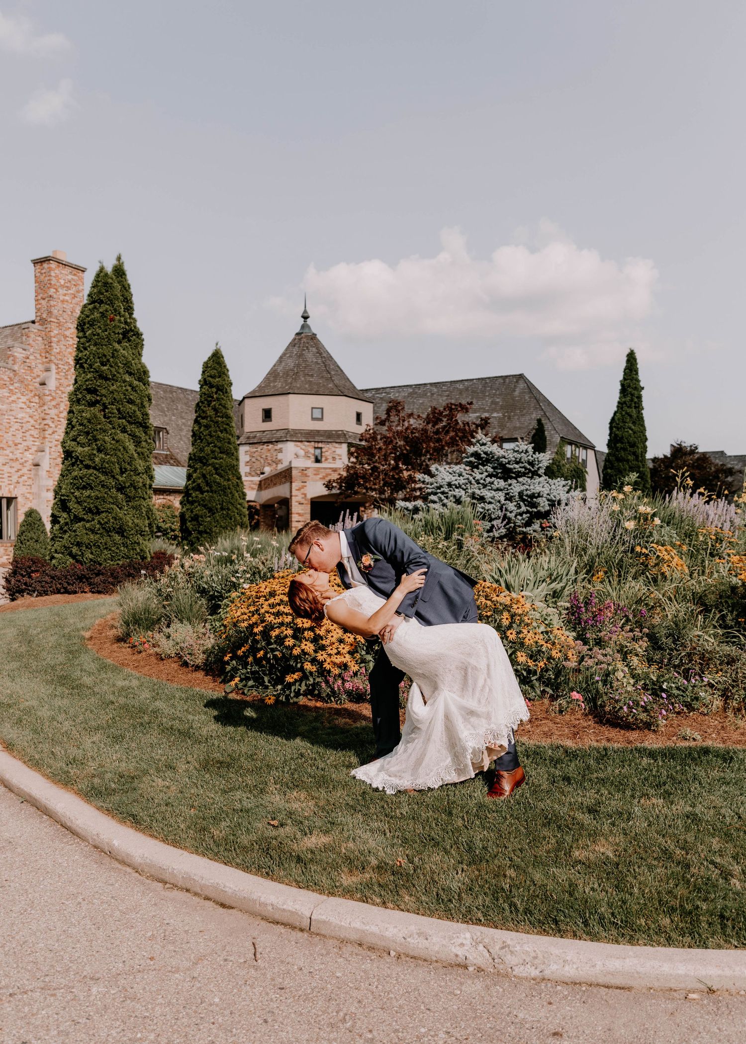 A romantic dip pose of newlyweds in a garden with blooming flowers and church architecture.