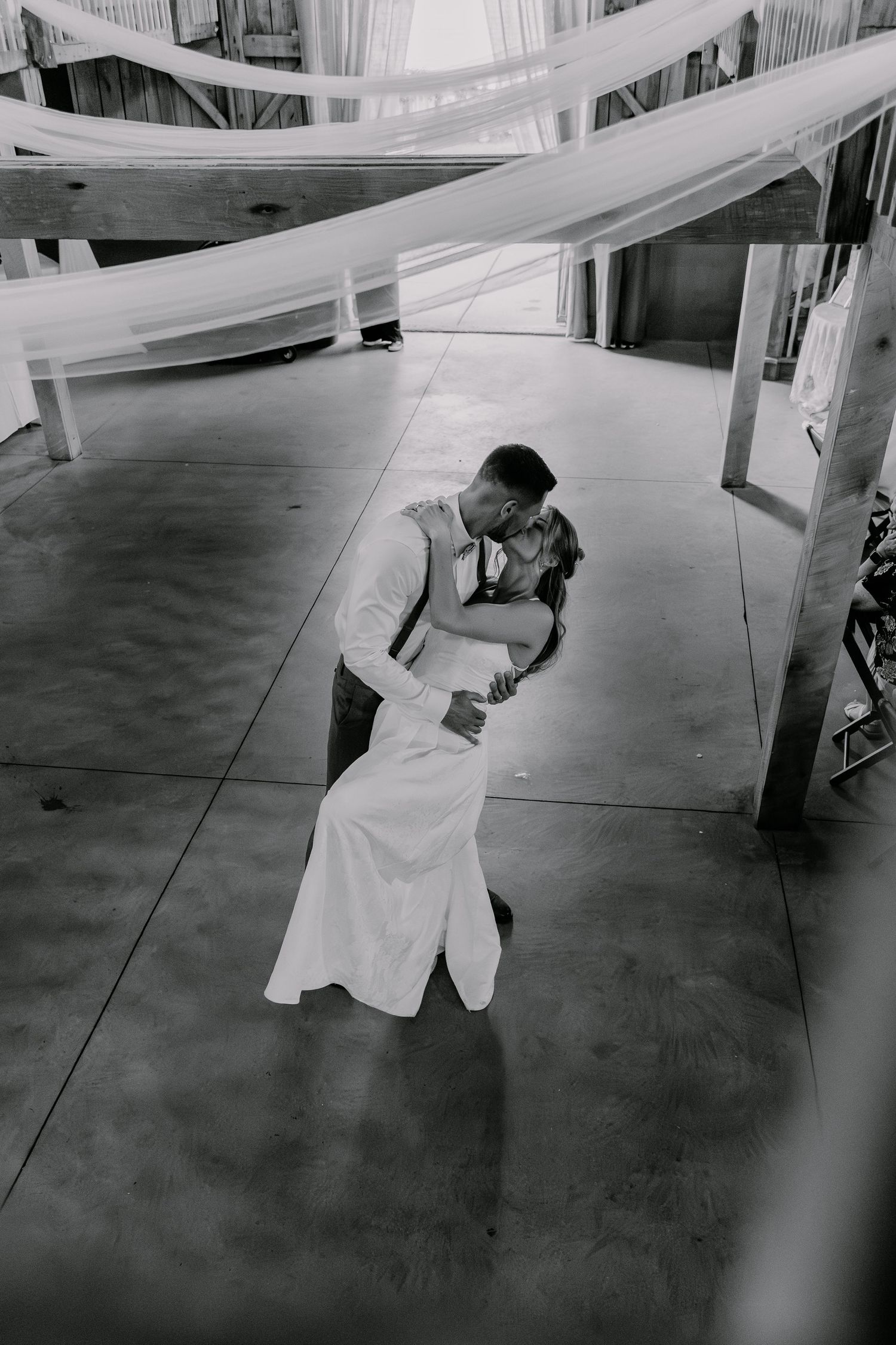 Black and white aerial shot of bride and groom sharing a romantic dip kiss on dance floor at wedding reception.