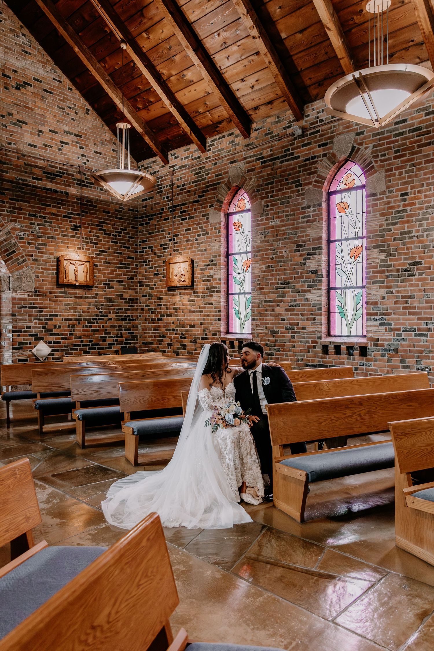 Beautiful rustic church interior with exposed brick walls, wooden pews and stained glass windows during a wedding ceremony.