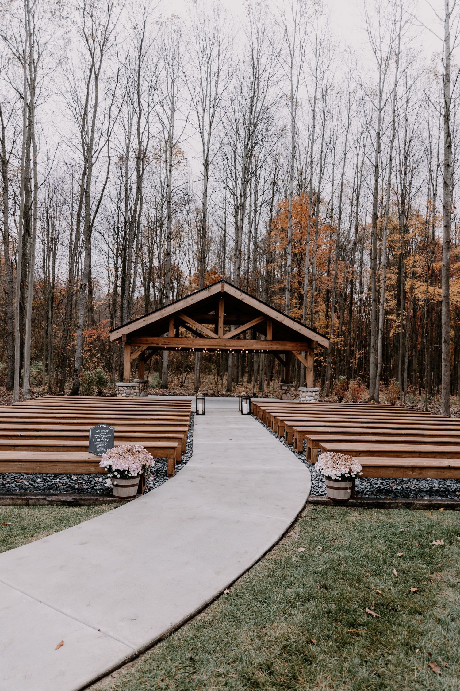 A rustic wooden wedding chapel with wooden benches surrounded by bare trees in autumn.