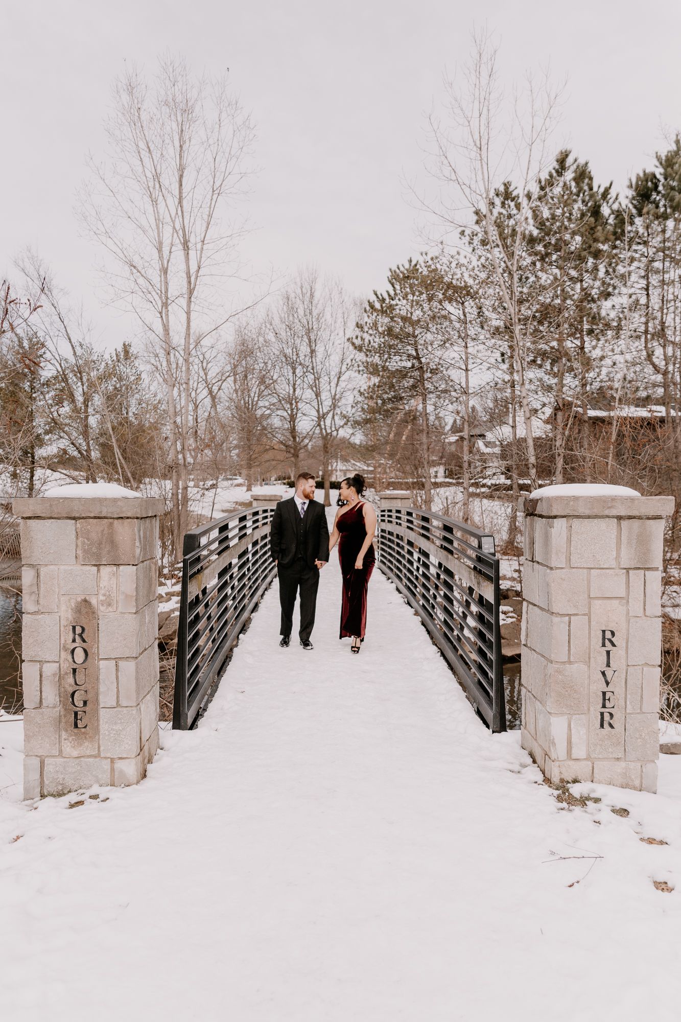 A couple standing on a snow-covered bridge during winter.