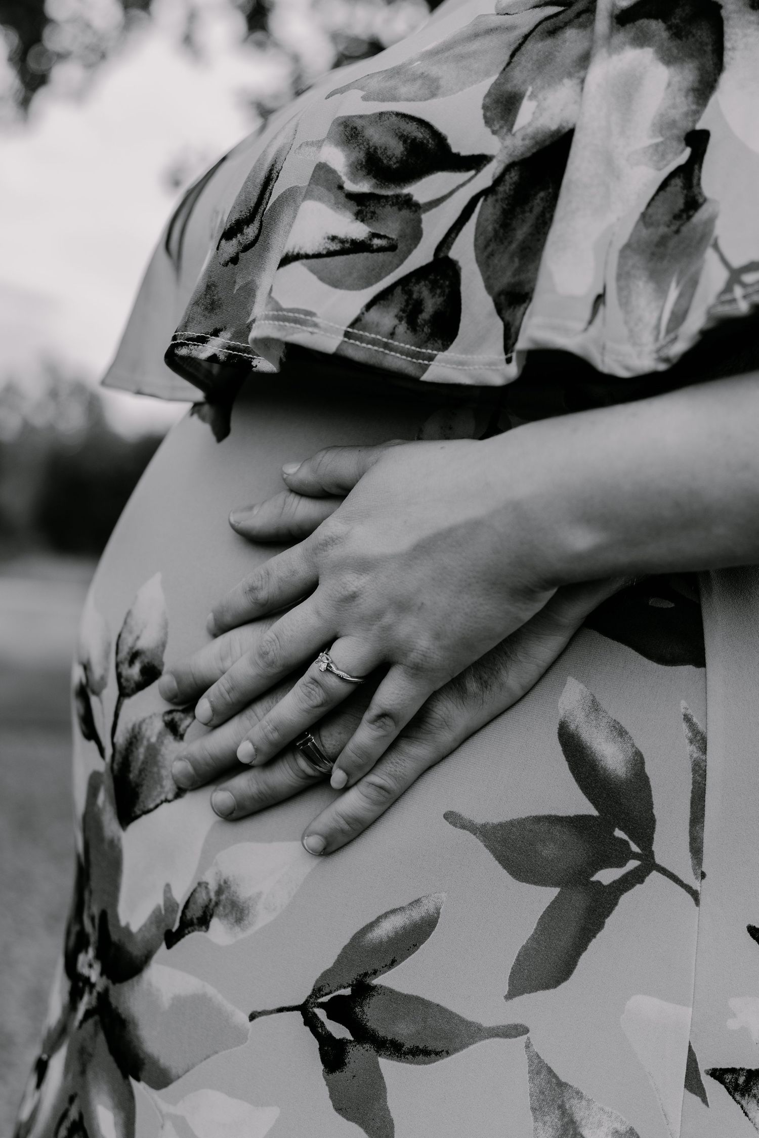 Close-up black and white photo of hands resting on a floral patterned dress fabric.