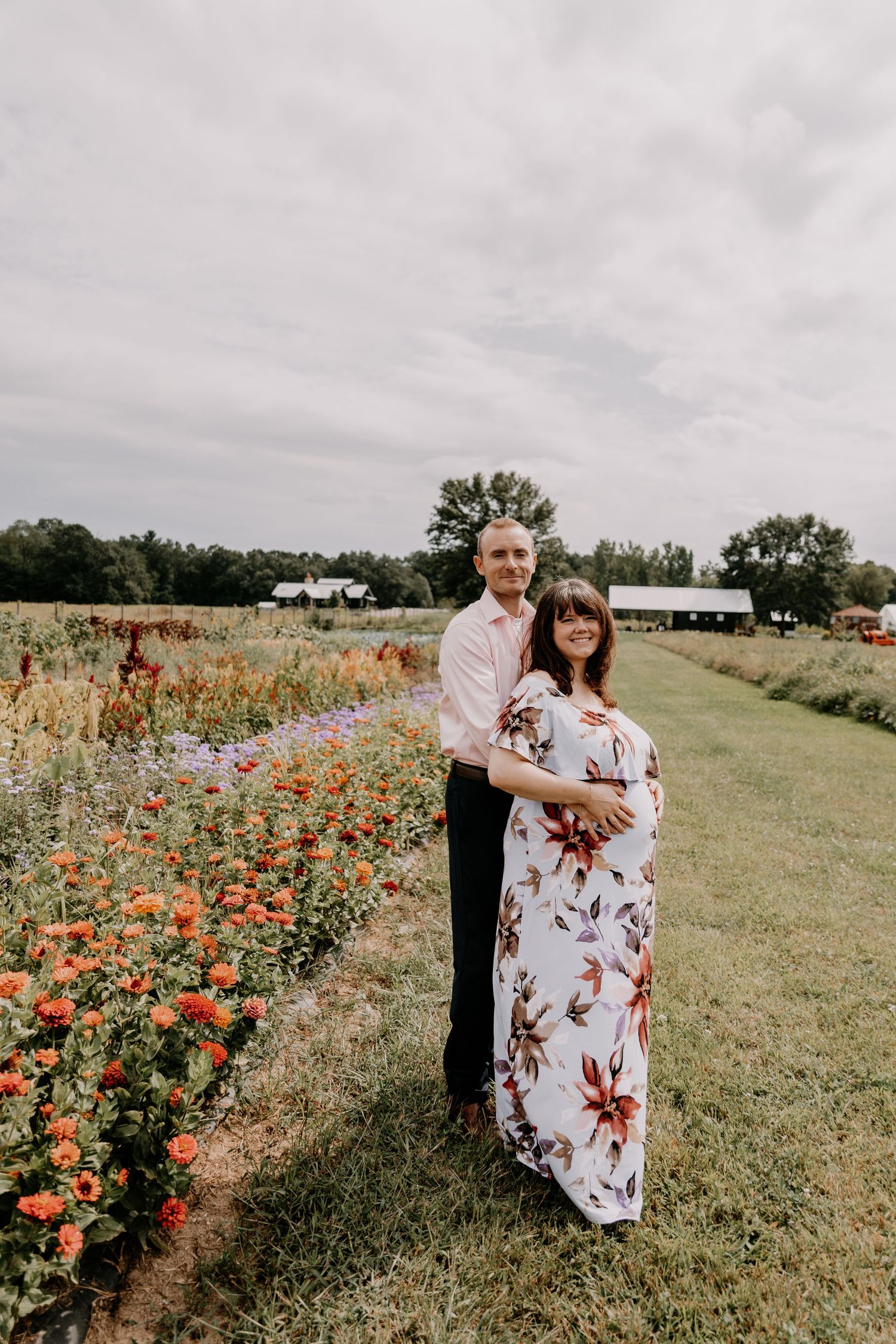 A couple poses among vibrant orange and purple wildflowers in a grassy field during a maternity photoshoot.