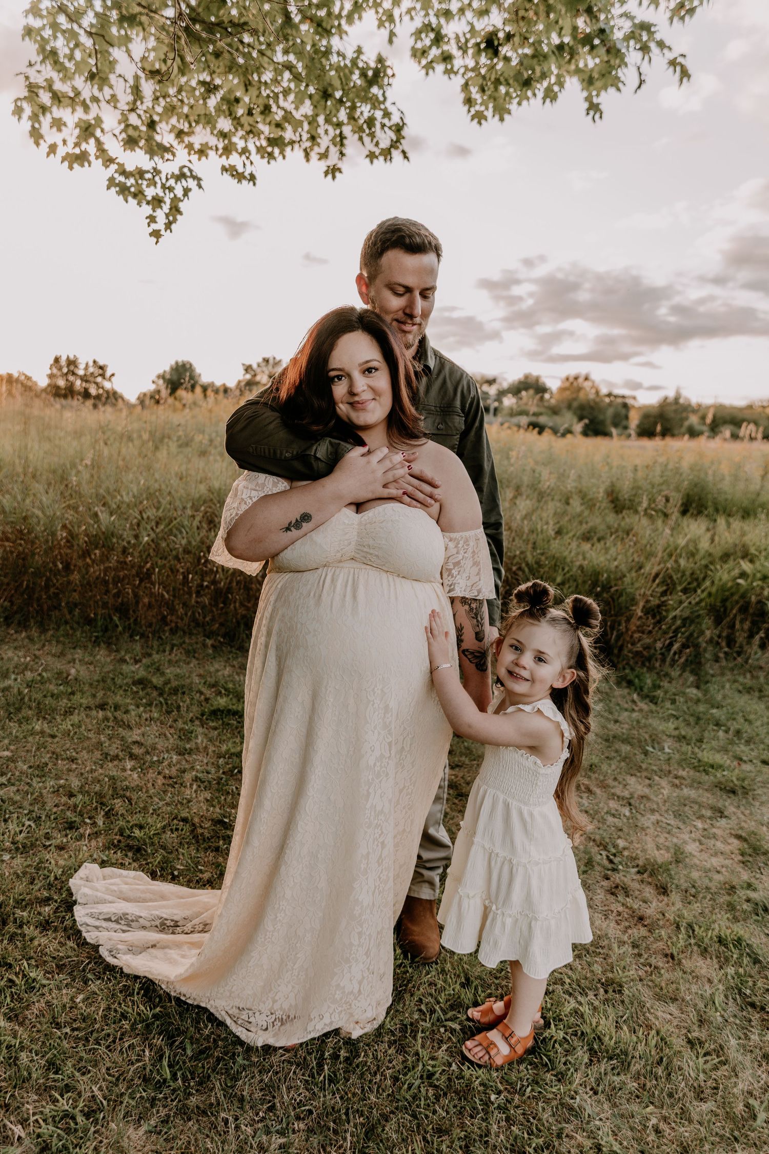 A heartwarming family moment captured in a field at sunset showing tender embraces and white dresses.