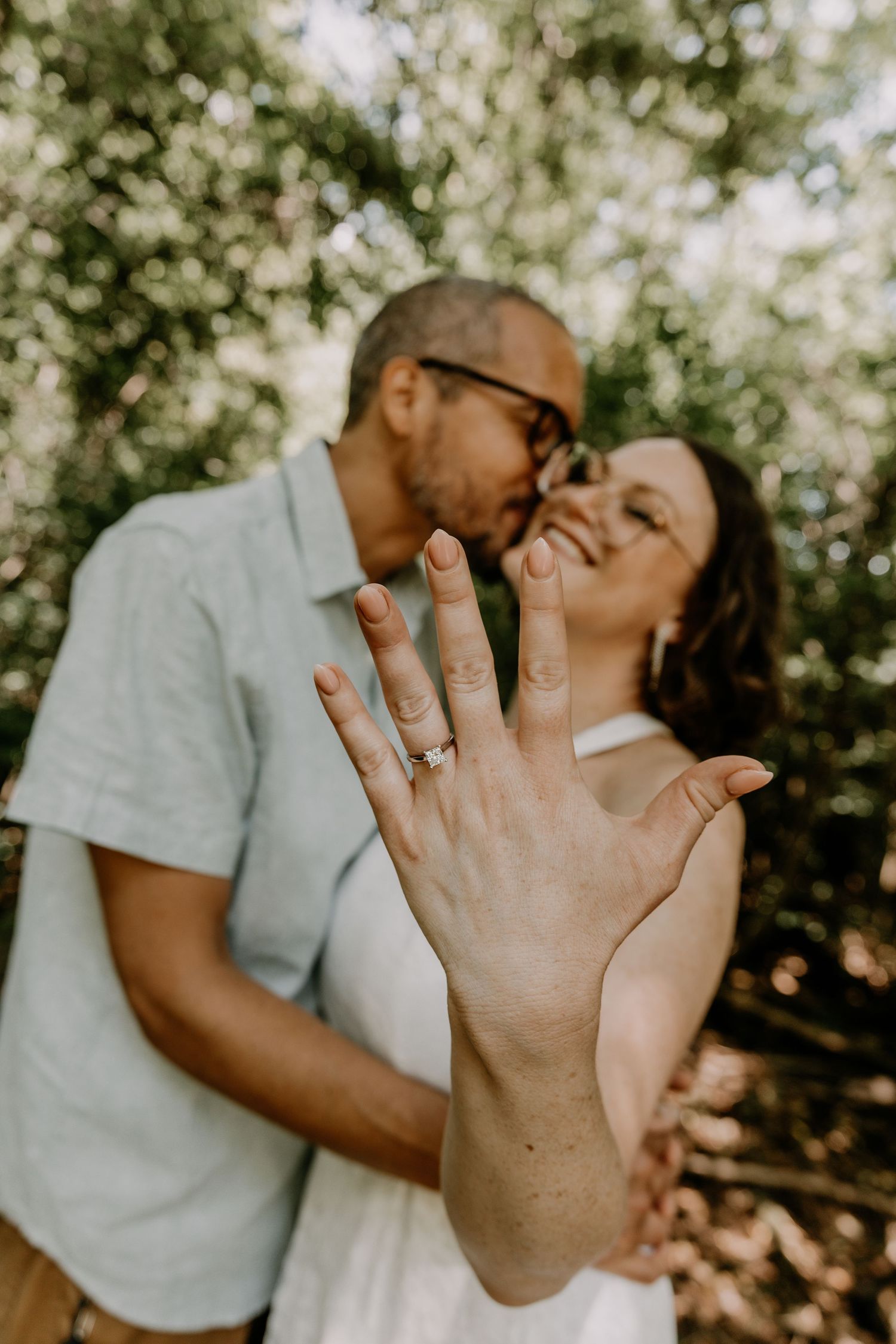 Newly engaged couple shares joyful moment outdoors while showing off engagement ring in natural sunlit setting.