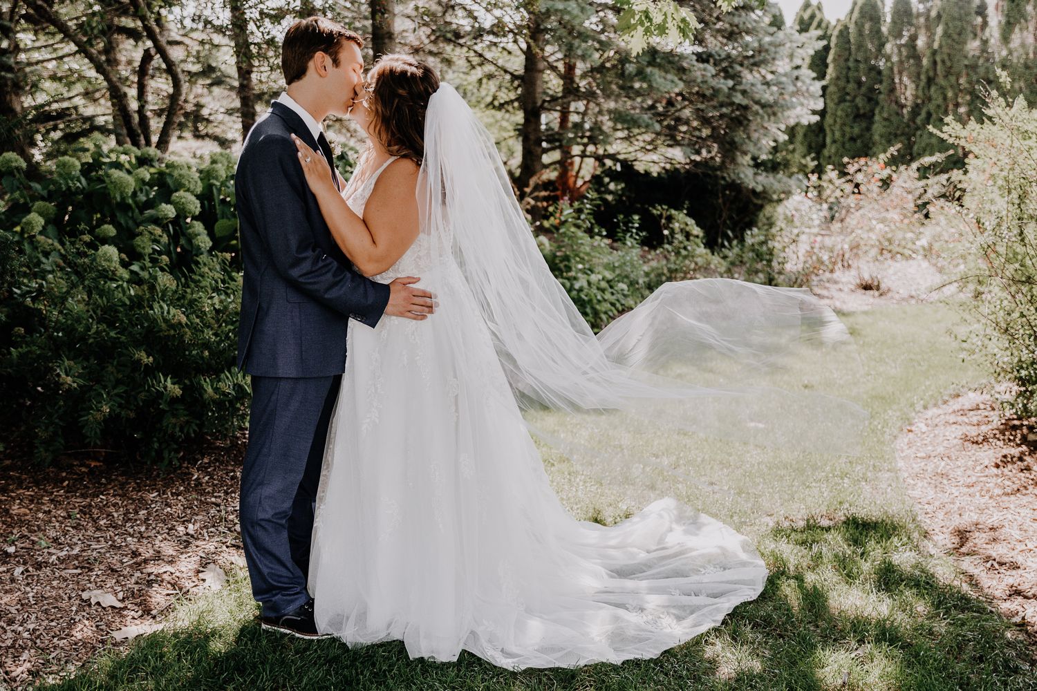Bride and groom embrace in dreamy garden setting with dramatic flowing wedding dress train.