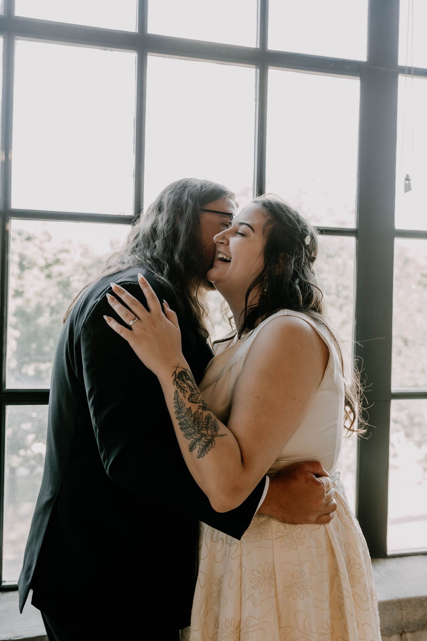 A joyful intimate moment between newlyweds laughing together by industrial windows.