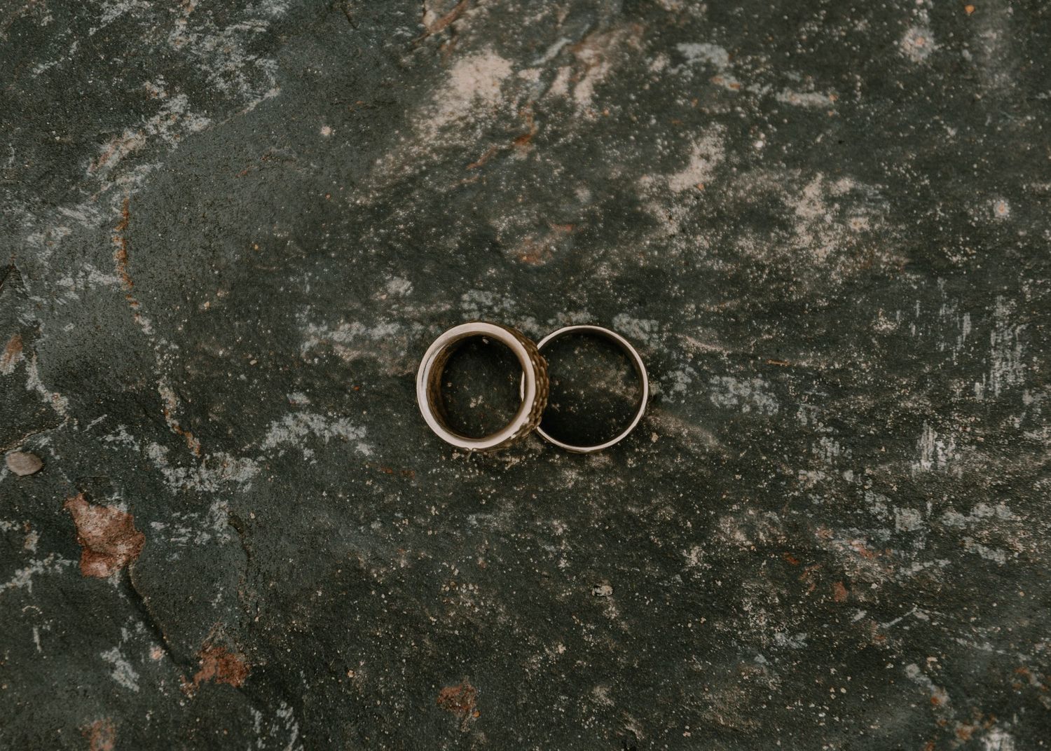 Two wedding rings photographed on dark textured stone surface.