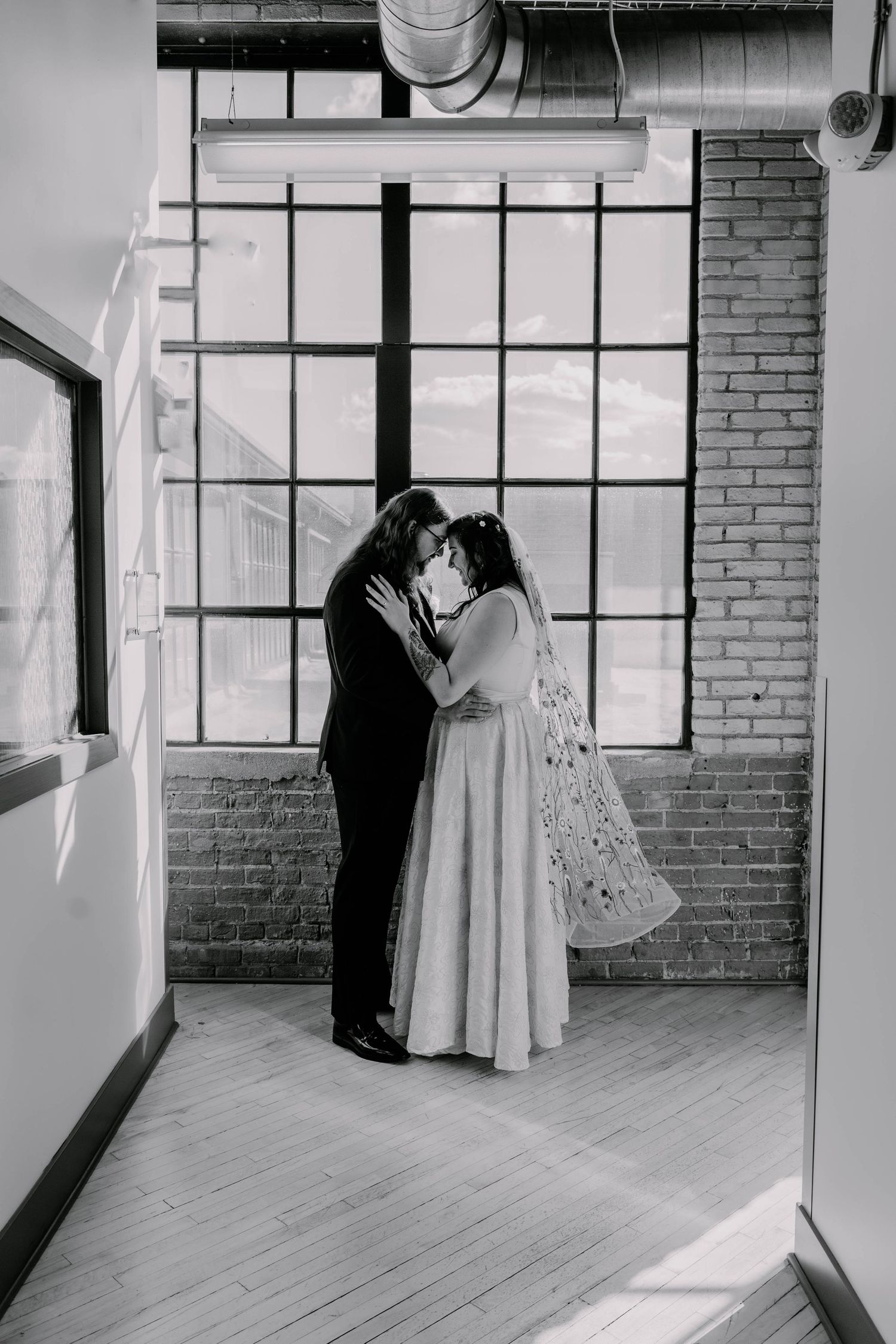A wedding dress is displayed in an elegant loft space with brick walls and large windows.
