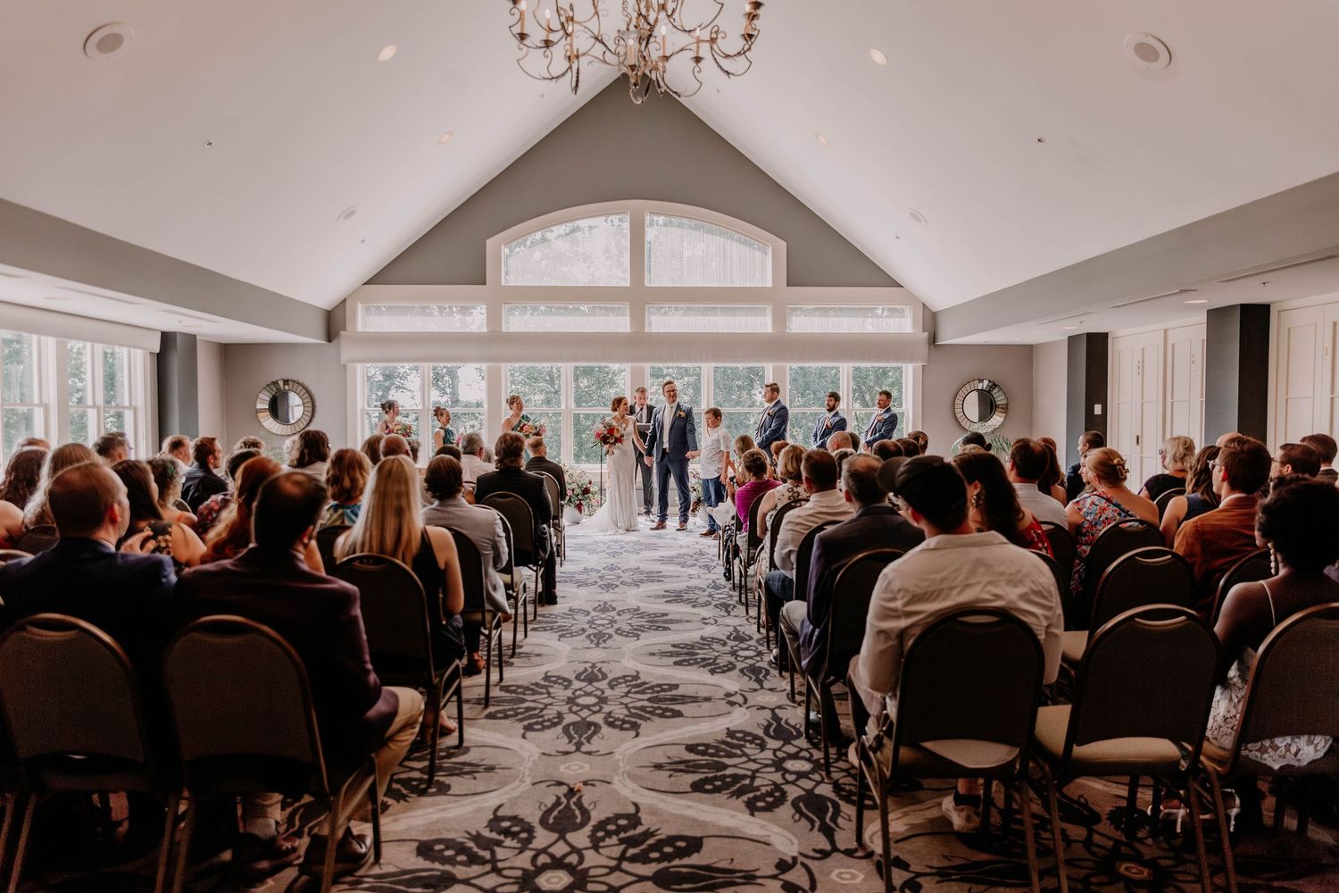 Wedding ceremony in a bright modern chapel with vaulted ceilings and rows of guests watching the couple.