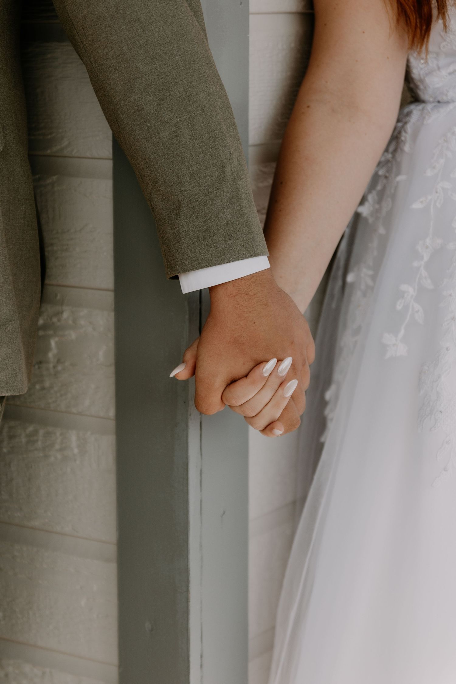 Close-up of newlyweds holding hands showing wedding rings and formal attire.