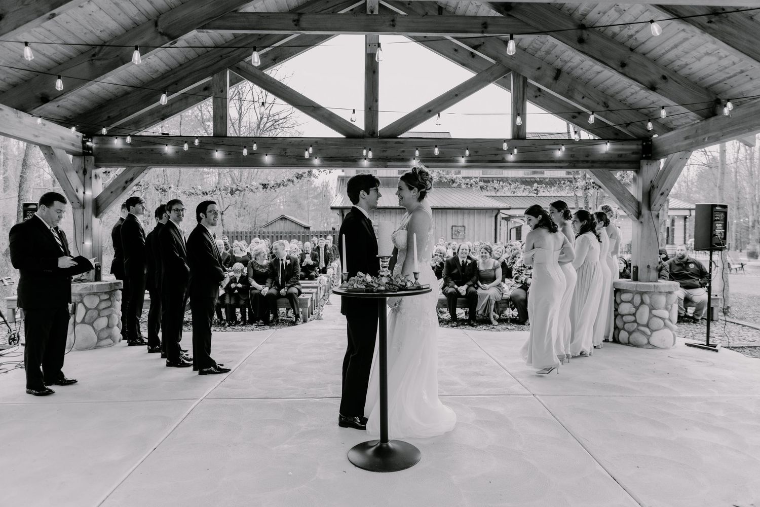 Black and white photo of wedding ceremony with bridal party and guests in rustic barn.
