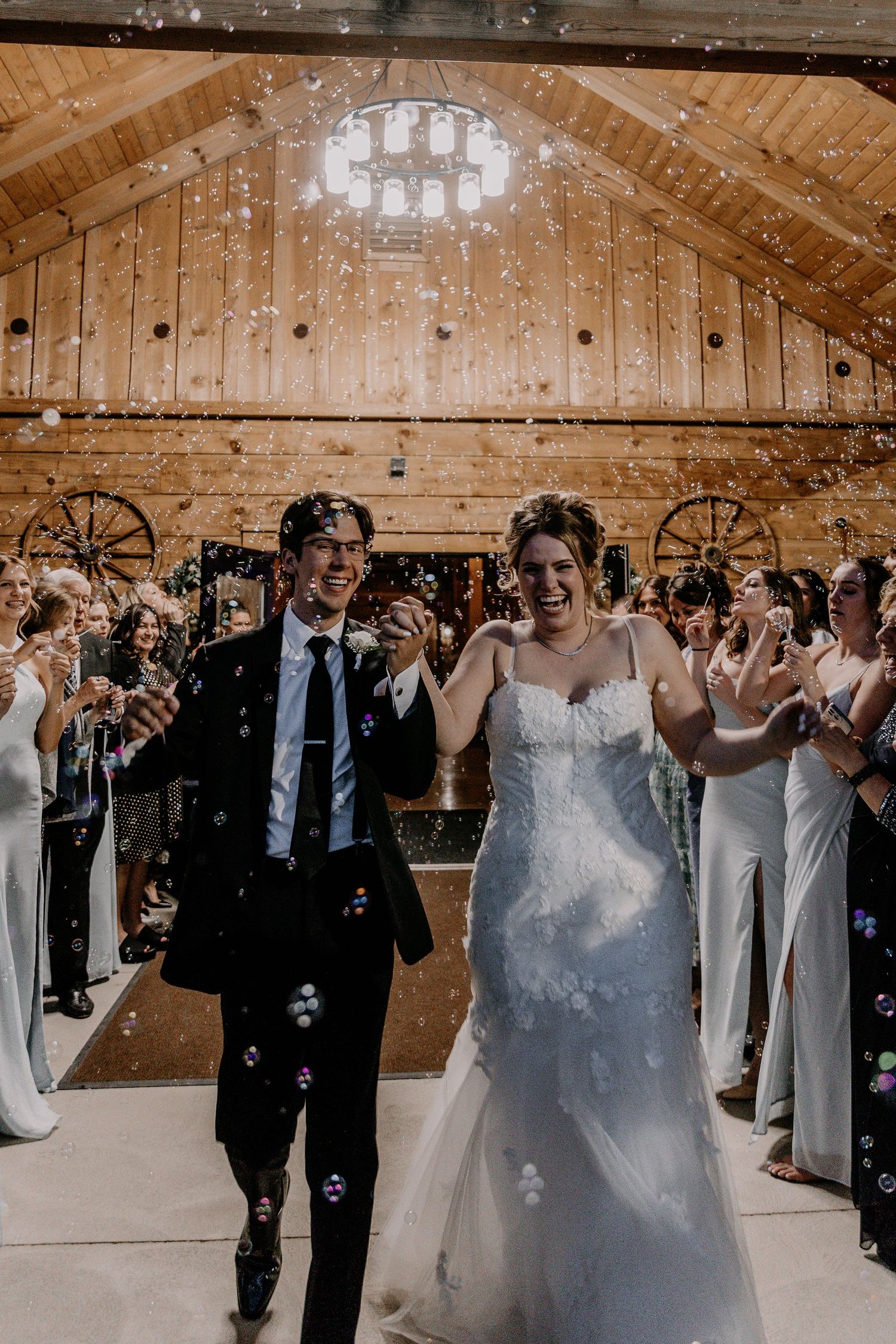 Wedding celebration in a wooden barn with guests blowing bubbles during the festivities.
