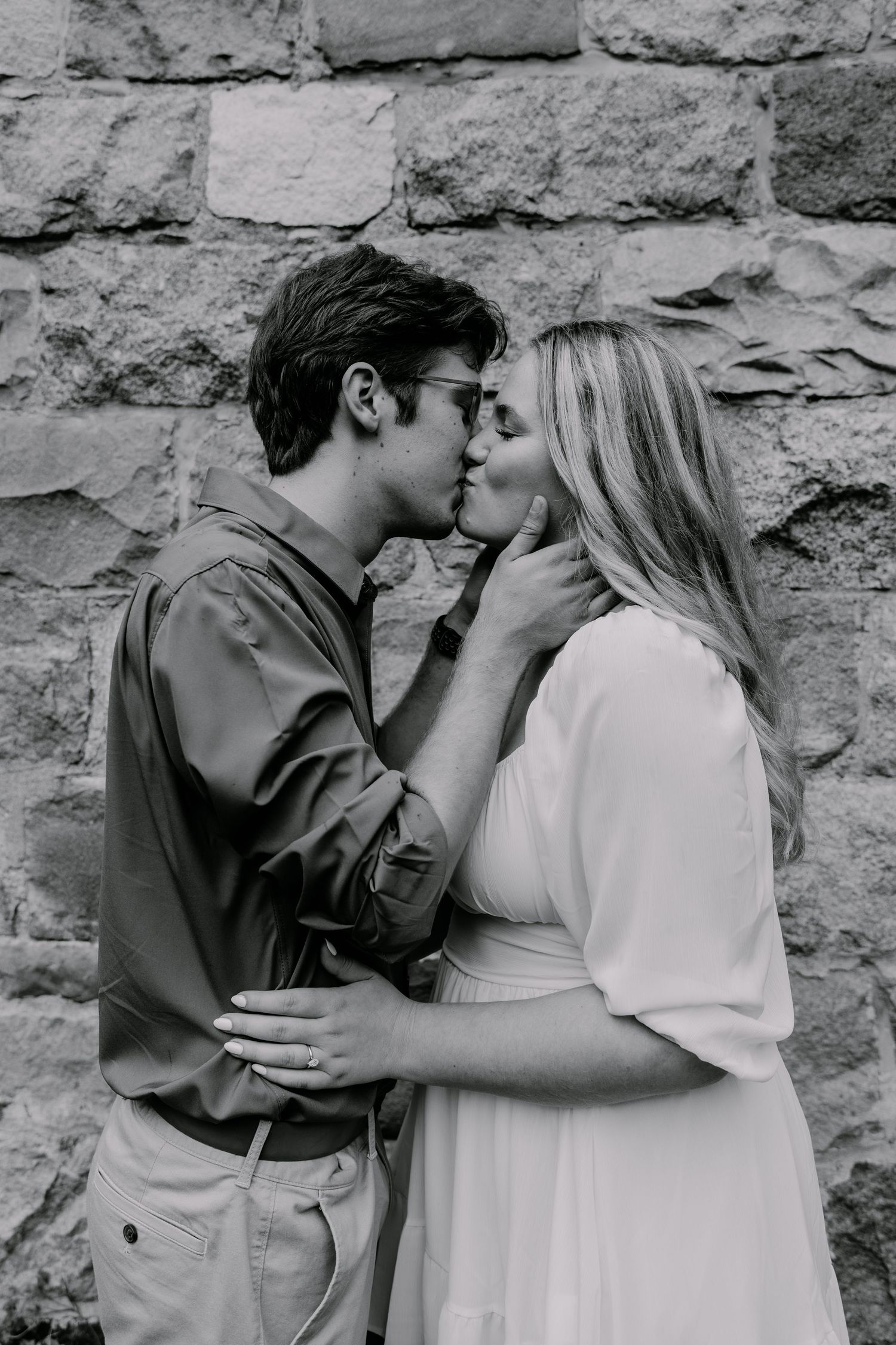 A couple shares a romantic kiss against a rustic stone wall background.