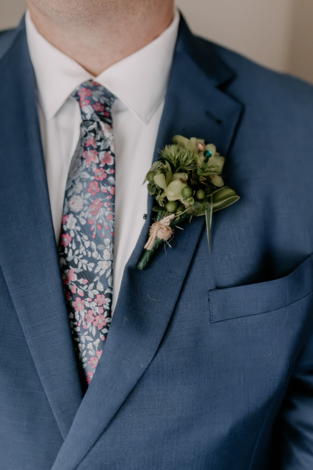 Elegant navy blue suit with floral patterned tie and green boutonniere displayed against neutral background.