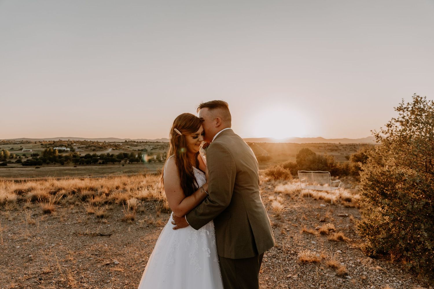 Couple embracing against a desert landscape backdrop during sunset.