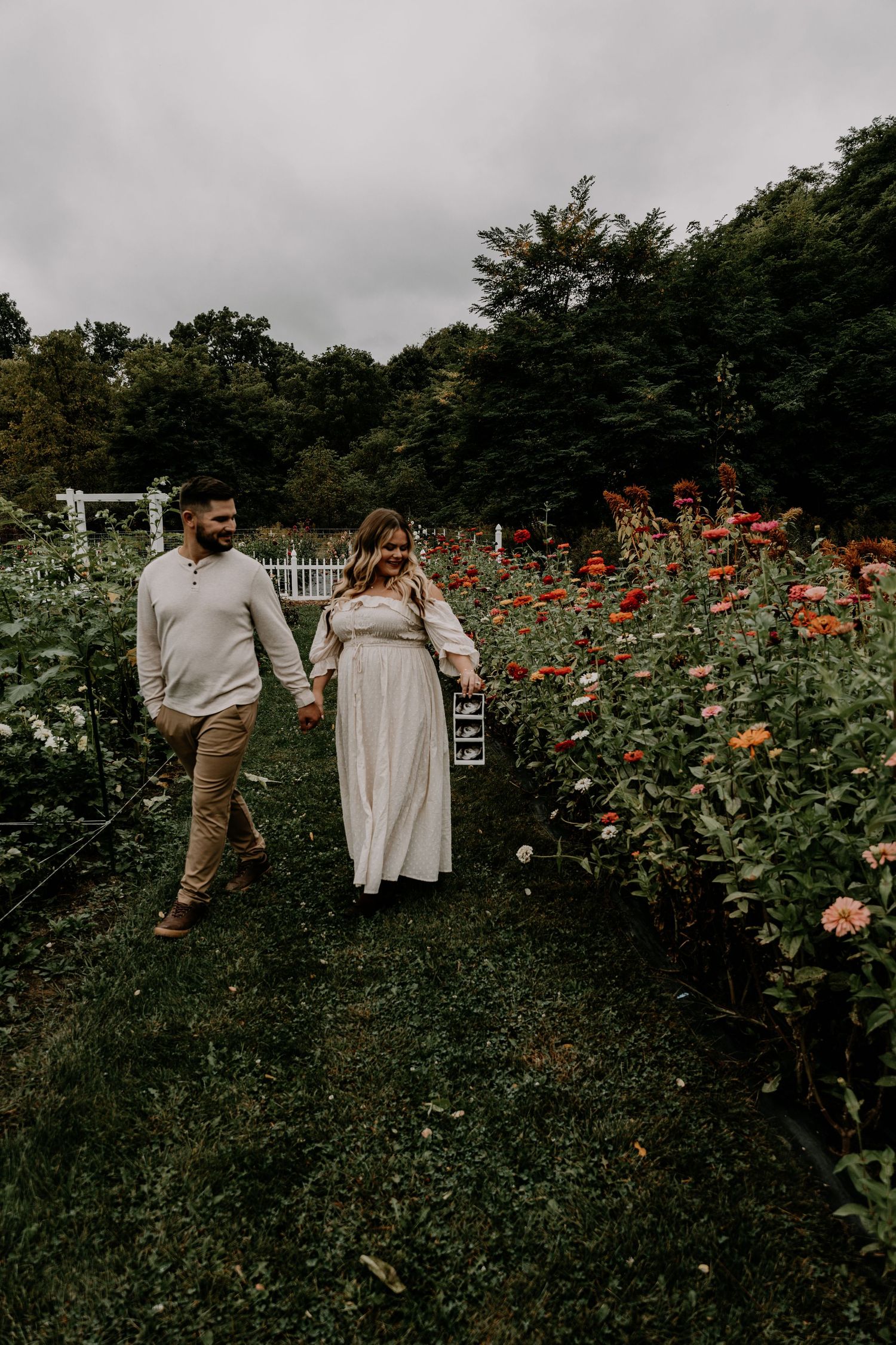 Couple celebrating in flower garden with dramatic cloudy sky backdrop.