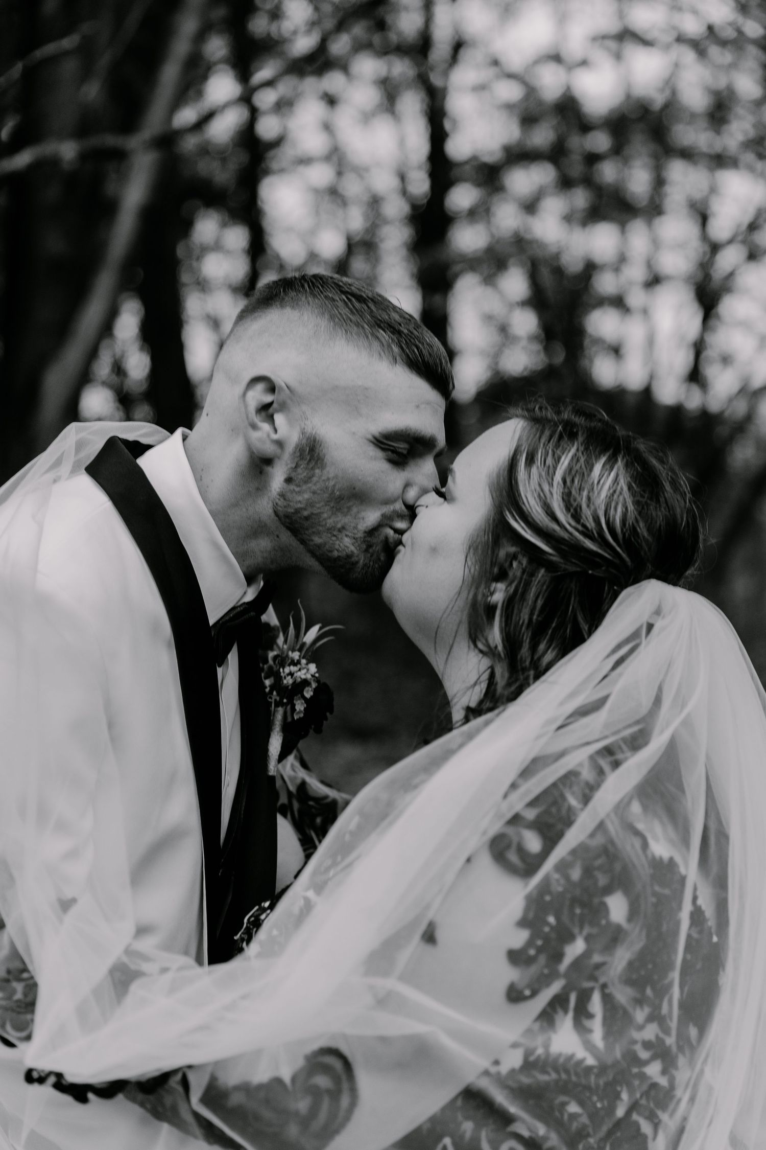 Black and white portrait of newlyweds sharing romantic kiss with lace veil detail.