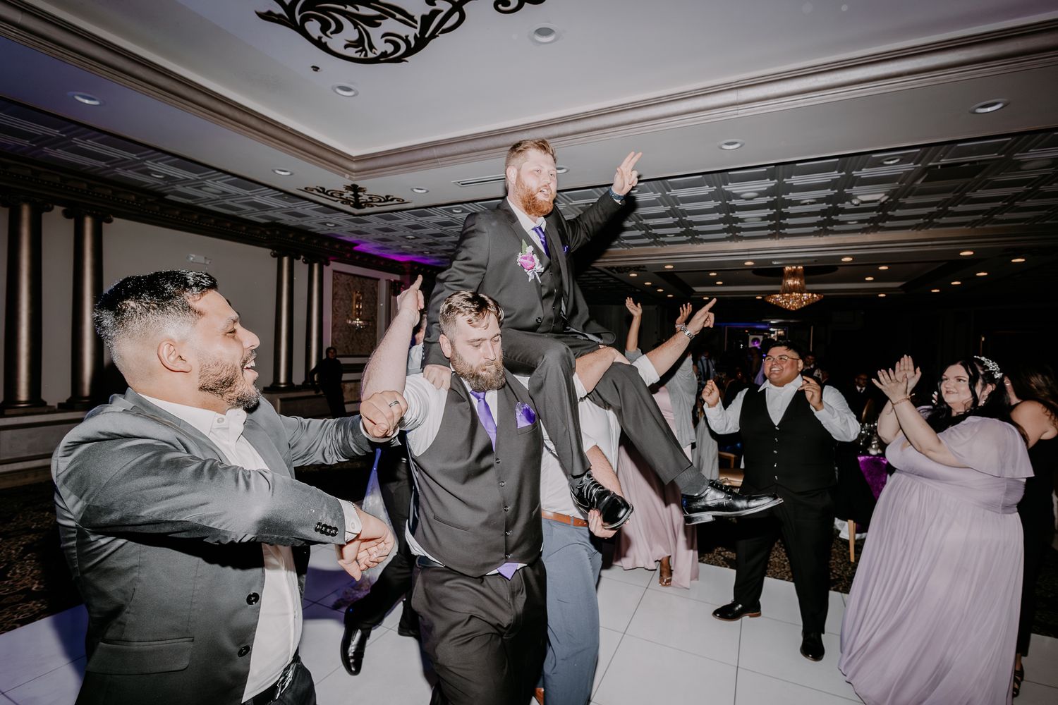Groom being lifted by guests during lively wedding reception celebrations.
