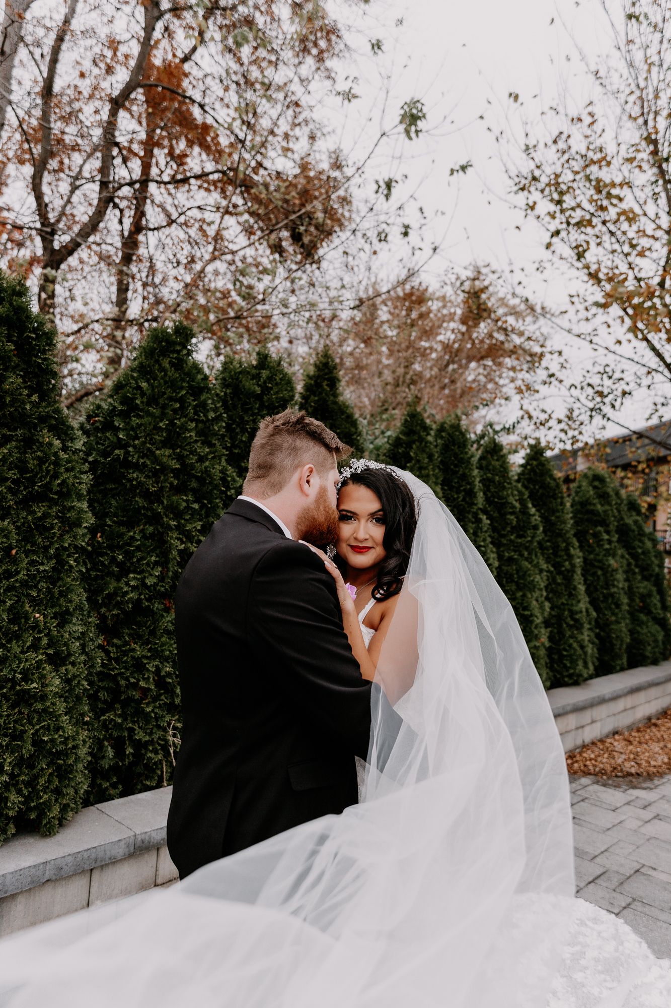 Romantic autumn wedding portrait with couple embracing against backdrop of evergreen trees.