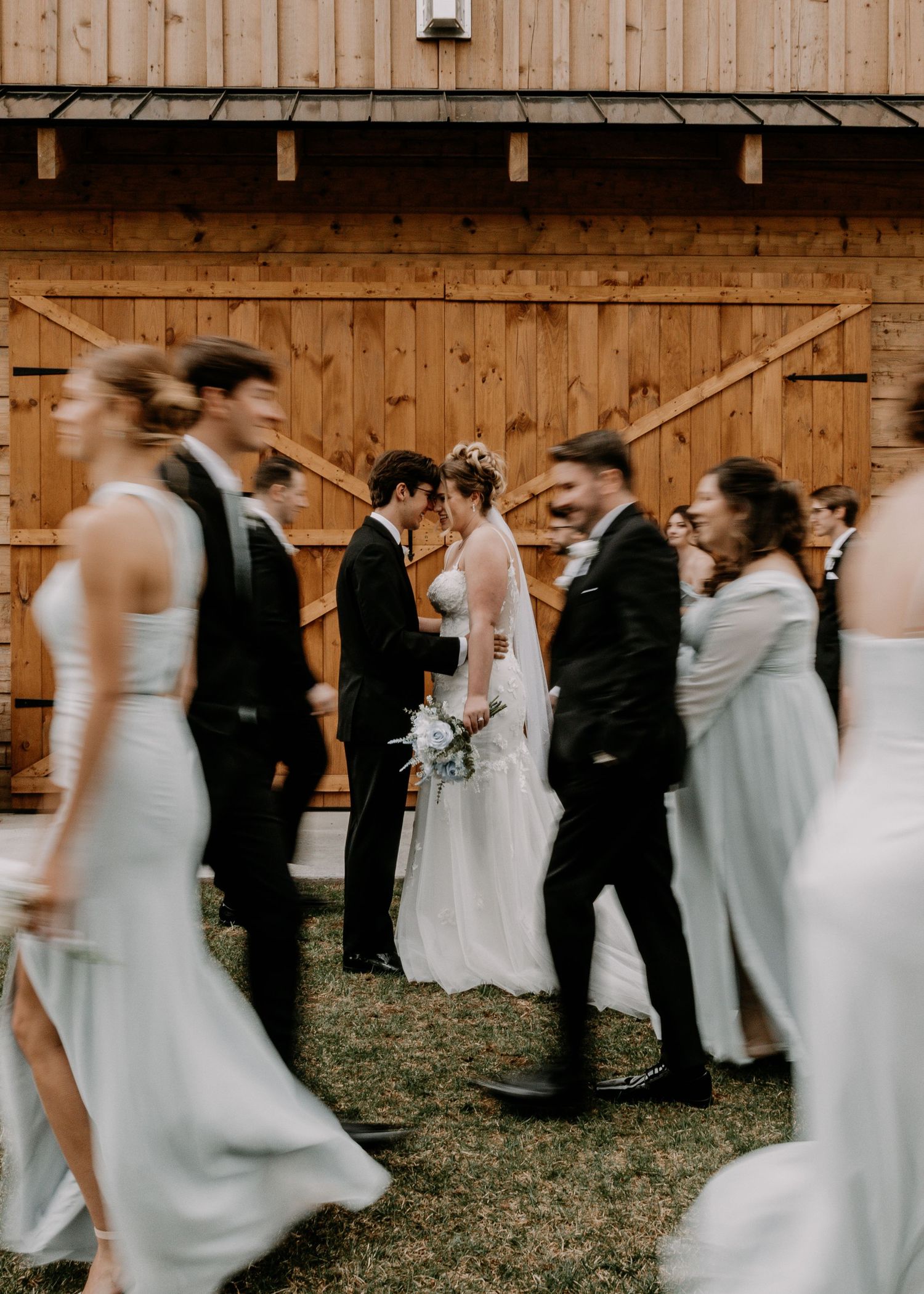 Motion-blurred candid photo of wedding party members walking outside rustic barn venue.
