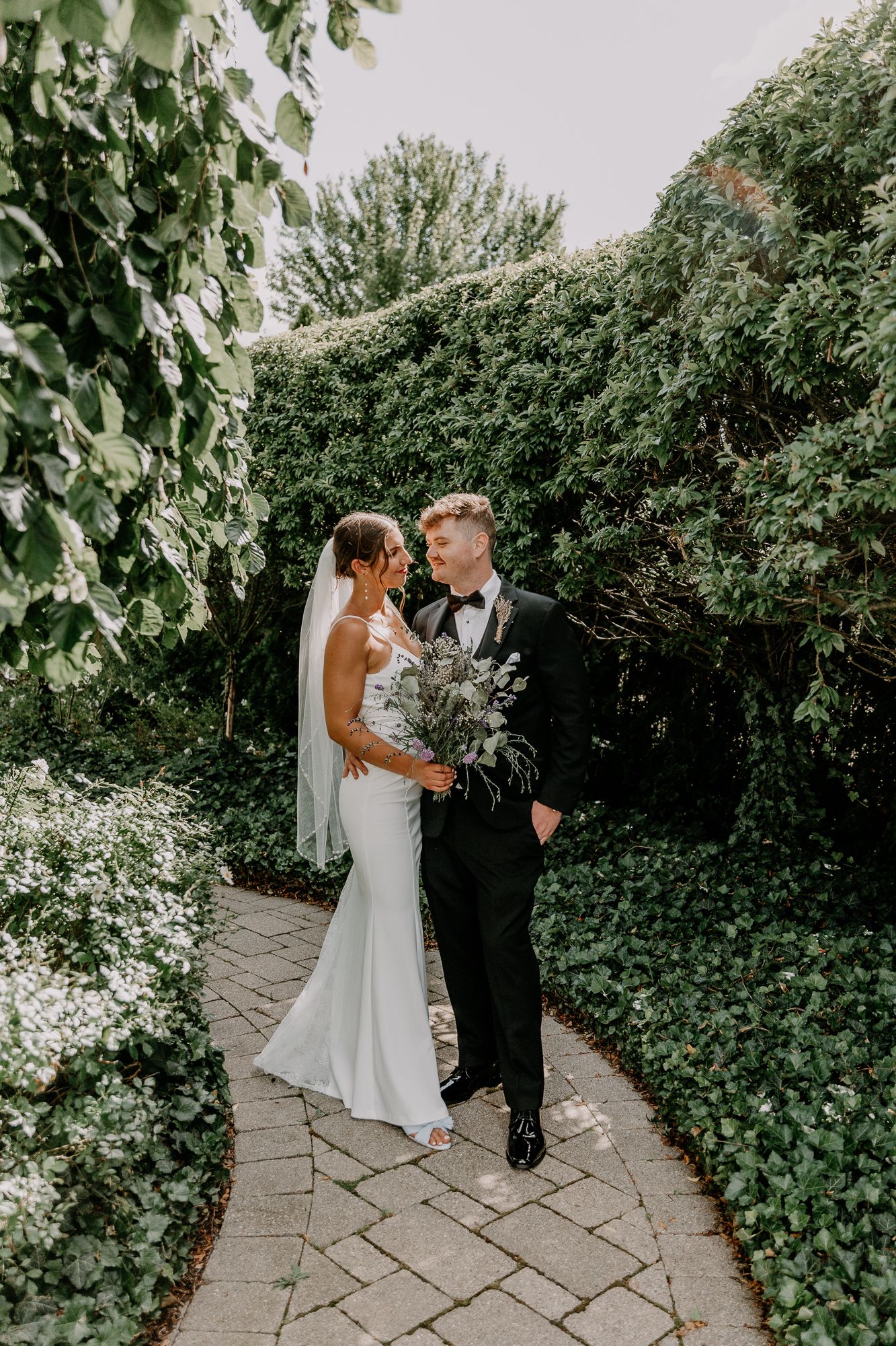 Couple poses on stone garden path surrounded by lush greenery.