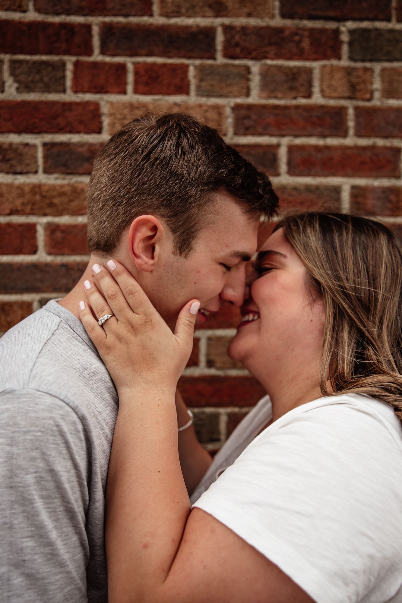 Close-up of couple sharing tender moment against rustic brick wall background.