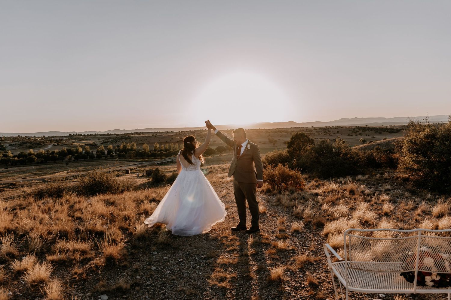 Newlyweds silhouetted against sunset on hilltop landscape.