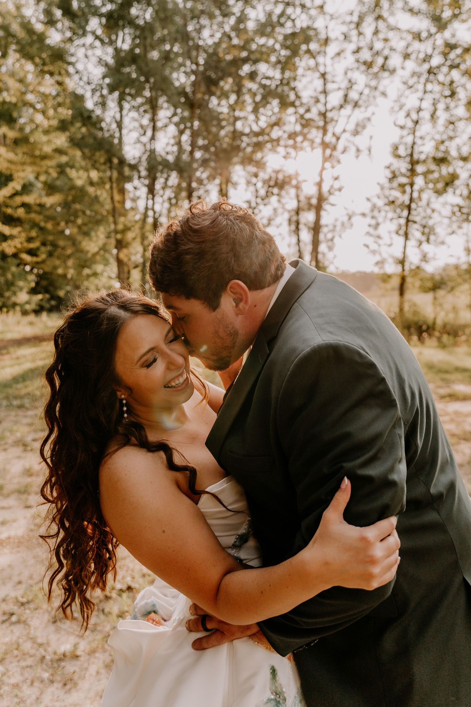 Bride and groom embracing romantically in a sunlit forest clearing during their outdoor wedding ceremony.