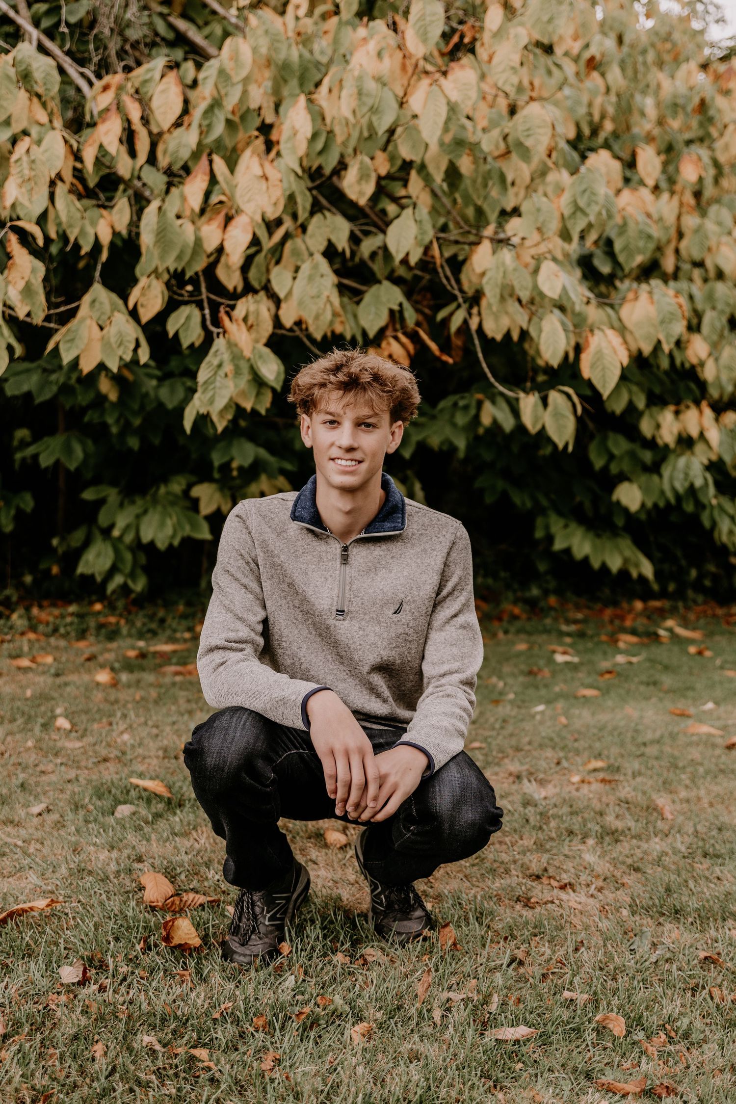 A person sits casually on autumn grass with fall foliage in the background.