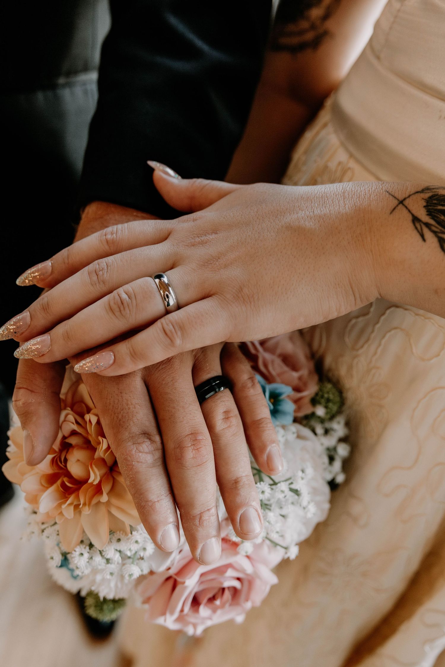 Wedding rings displayed on hands resting on a bouquet with pink roses and white flowers.