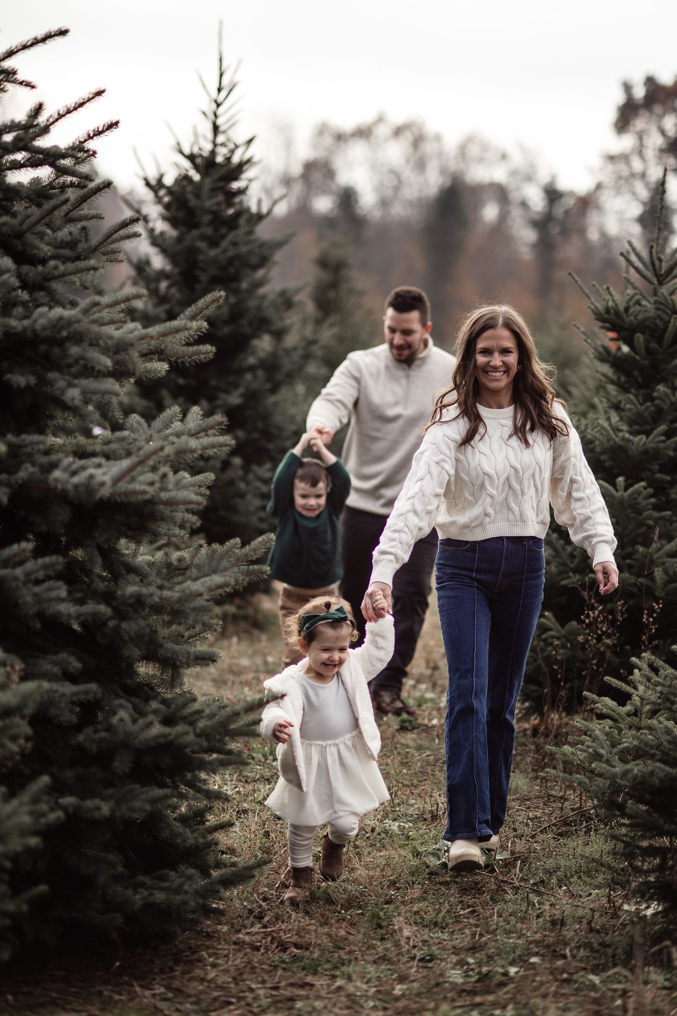 Family walking together through rows of Christmas trees on a cloudy day.
