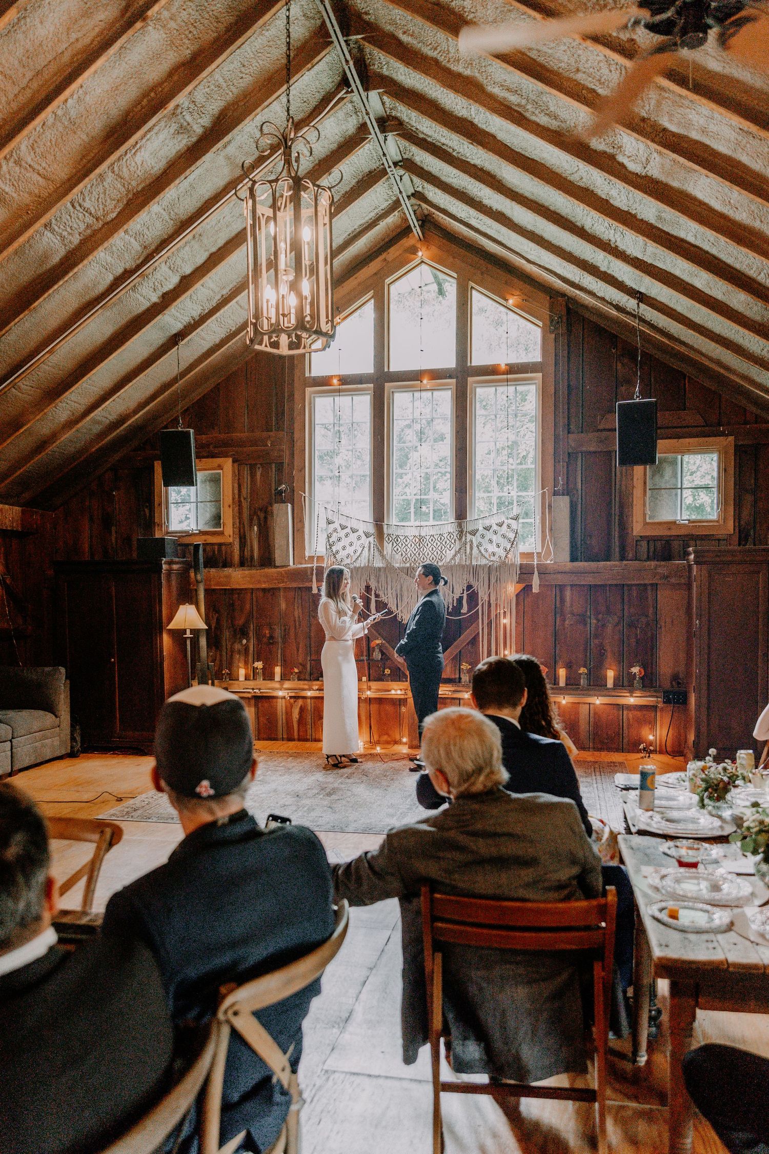 Wedding ceremony in rustic wooden chapel with exposed beams and hanging lights.