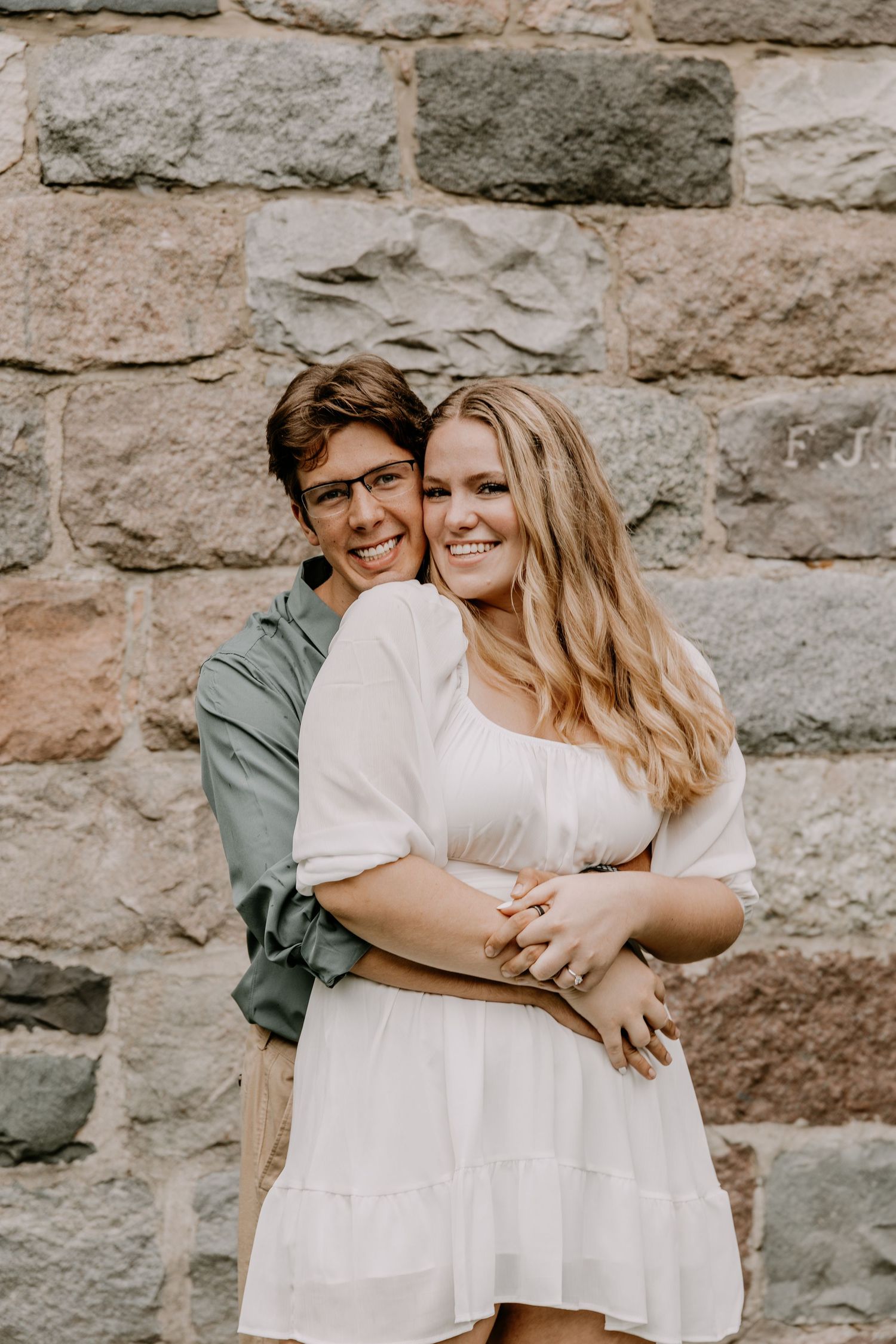Happy couple embracing in front of rustic stone wall during romantic photoshoot.