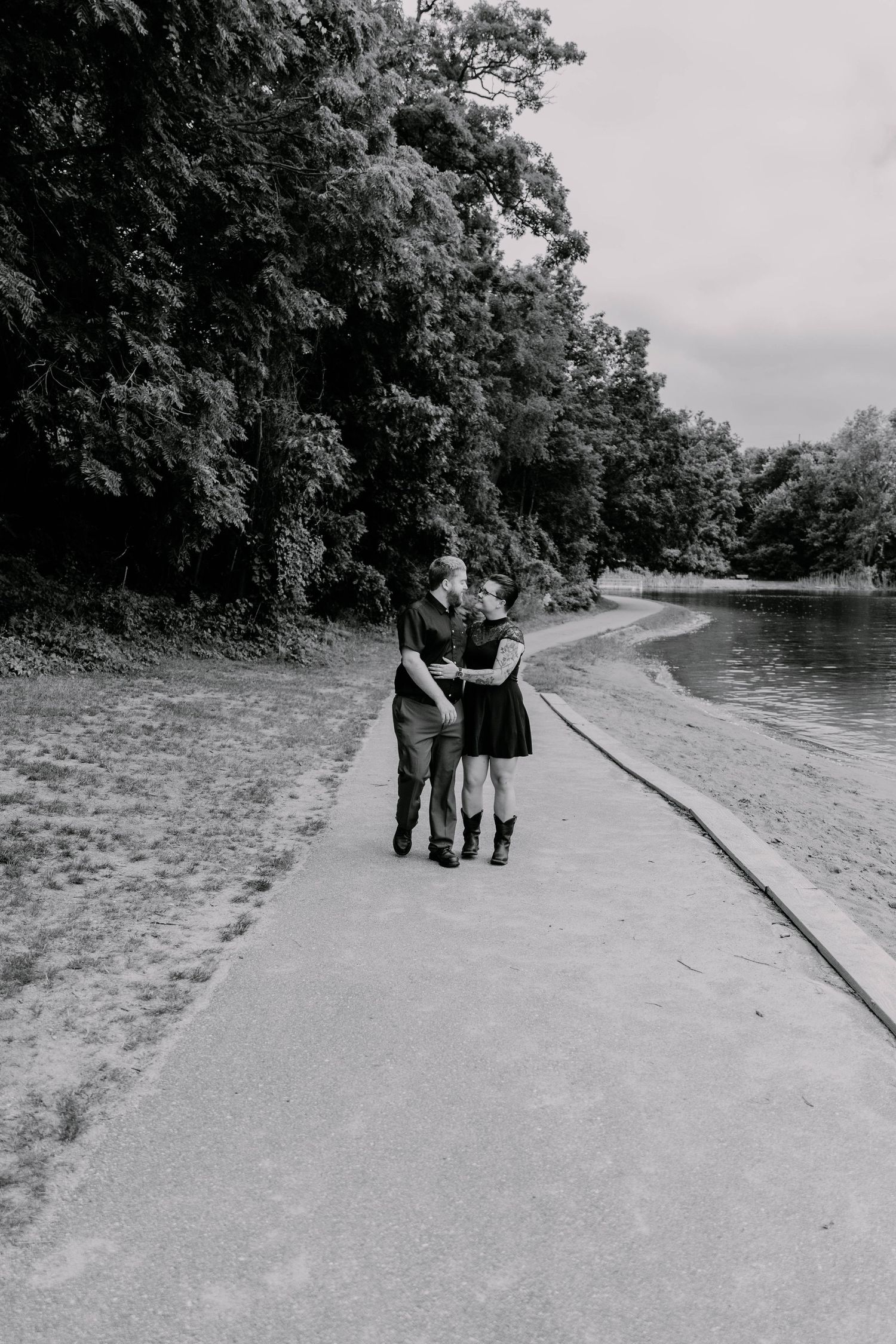 A couple embraces while standing on a path beside a scenic lake.
