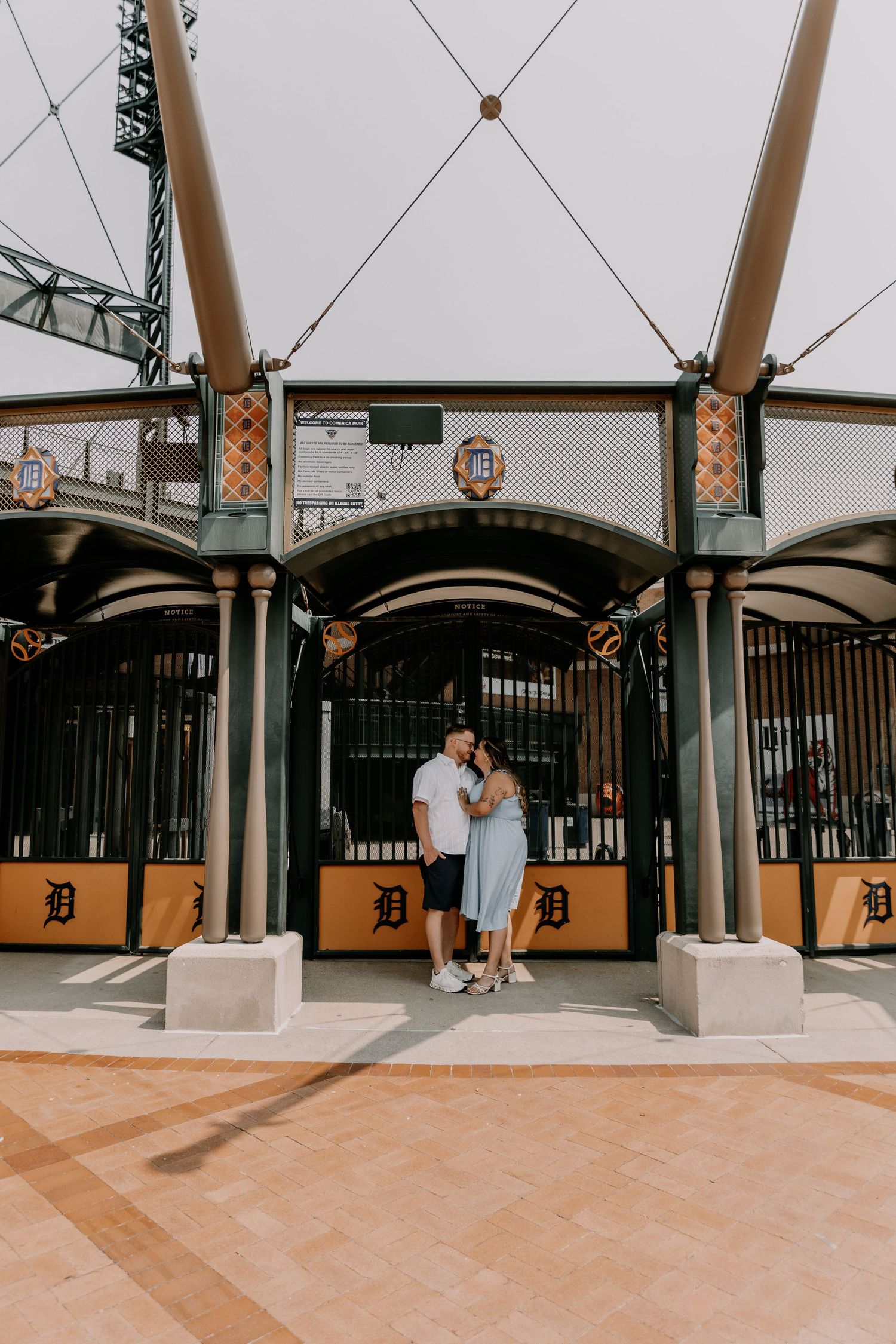 Baseball stadium engagement photo at Detroit Tigers Comerica Park showing couple under architectural entrance canopy.
