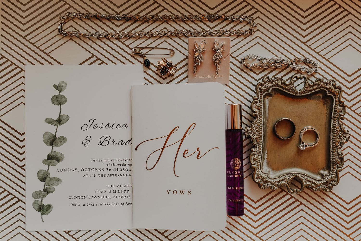 Wedding invitation suite with calligraphy, eucalyptus leaves, and gold chevron pattern displayed on wooden surface.