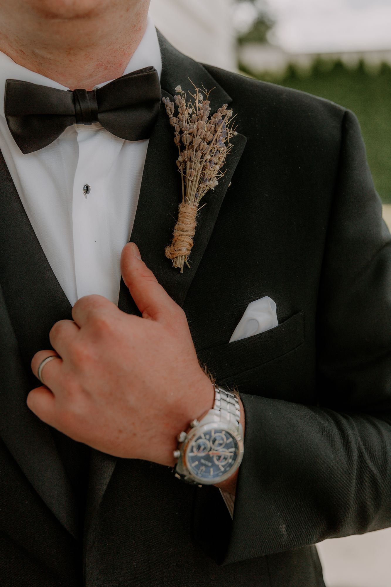 Close-up detail of groom's boutonniere, bow tie, and watch with classic black tuxedo.