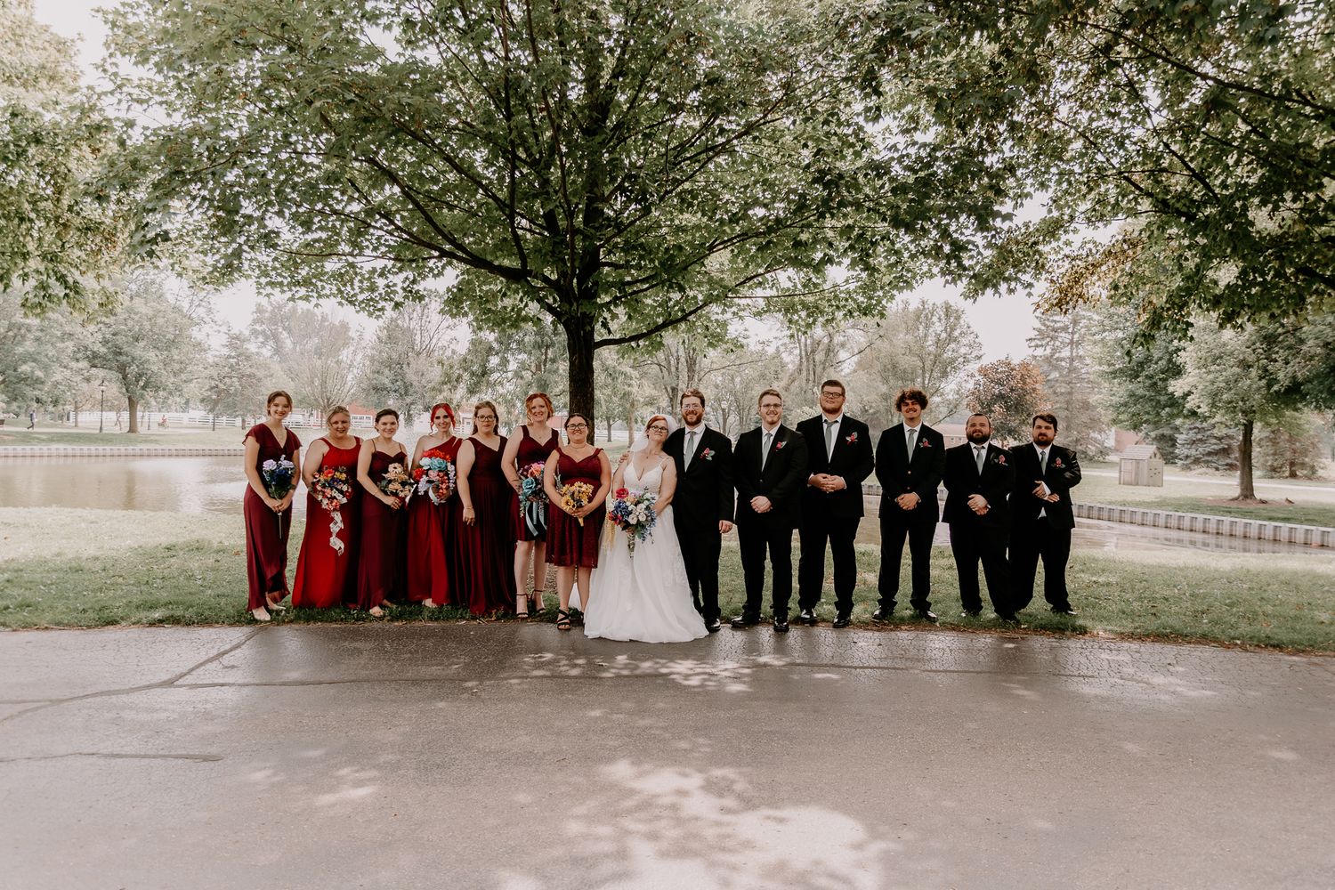Wedding party poses outdoors with bridesmaids in burgundy and groomsmen in black.