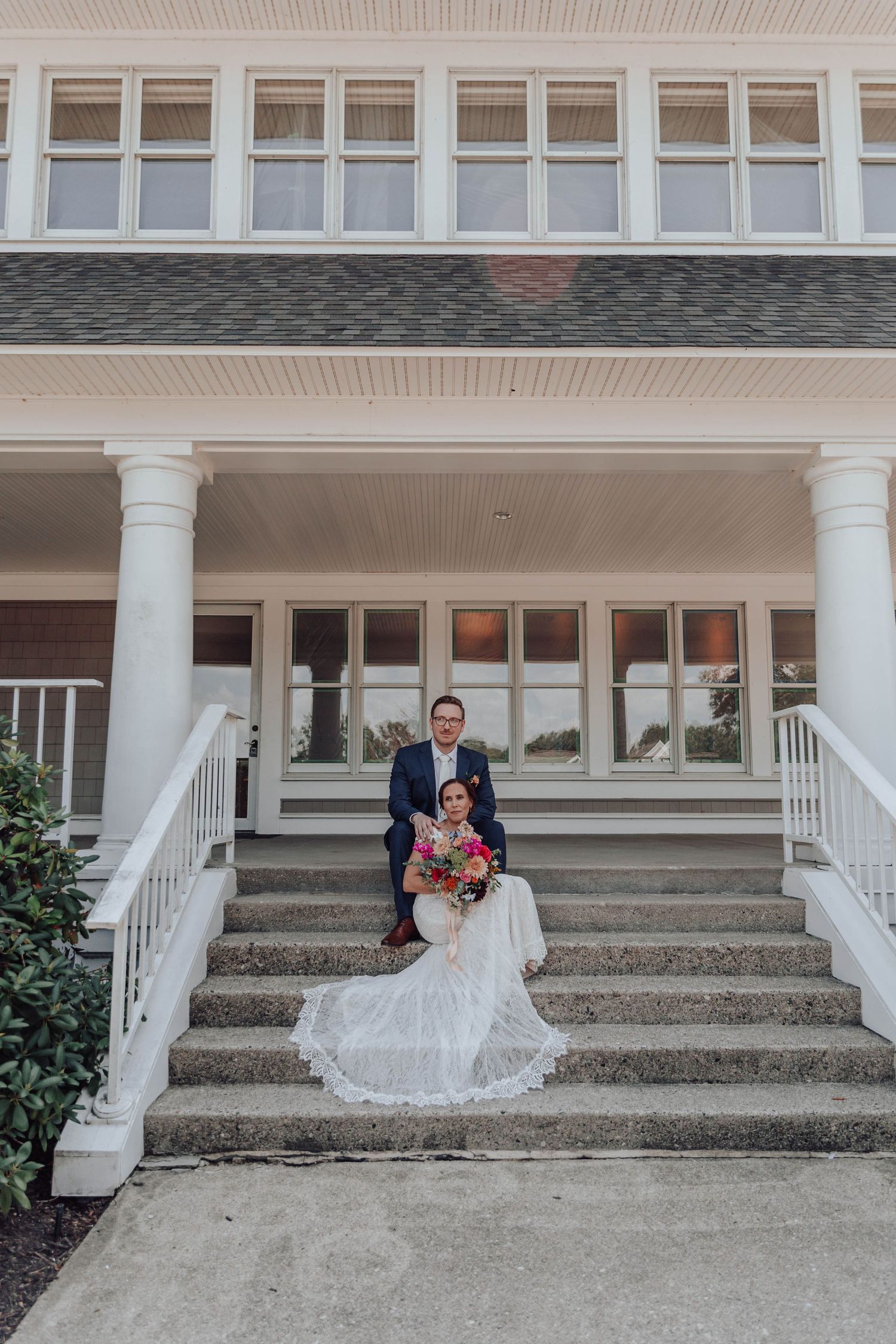 Newlyweds sitting on white building steps with classic colonial architecture and columns.