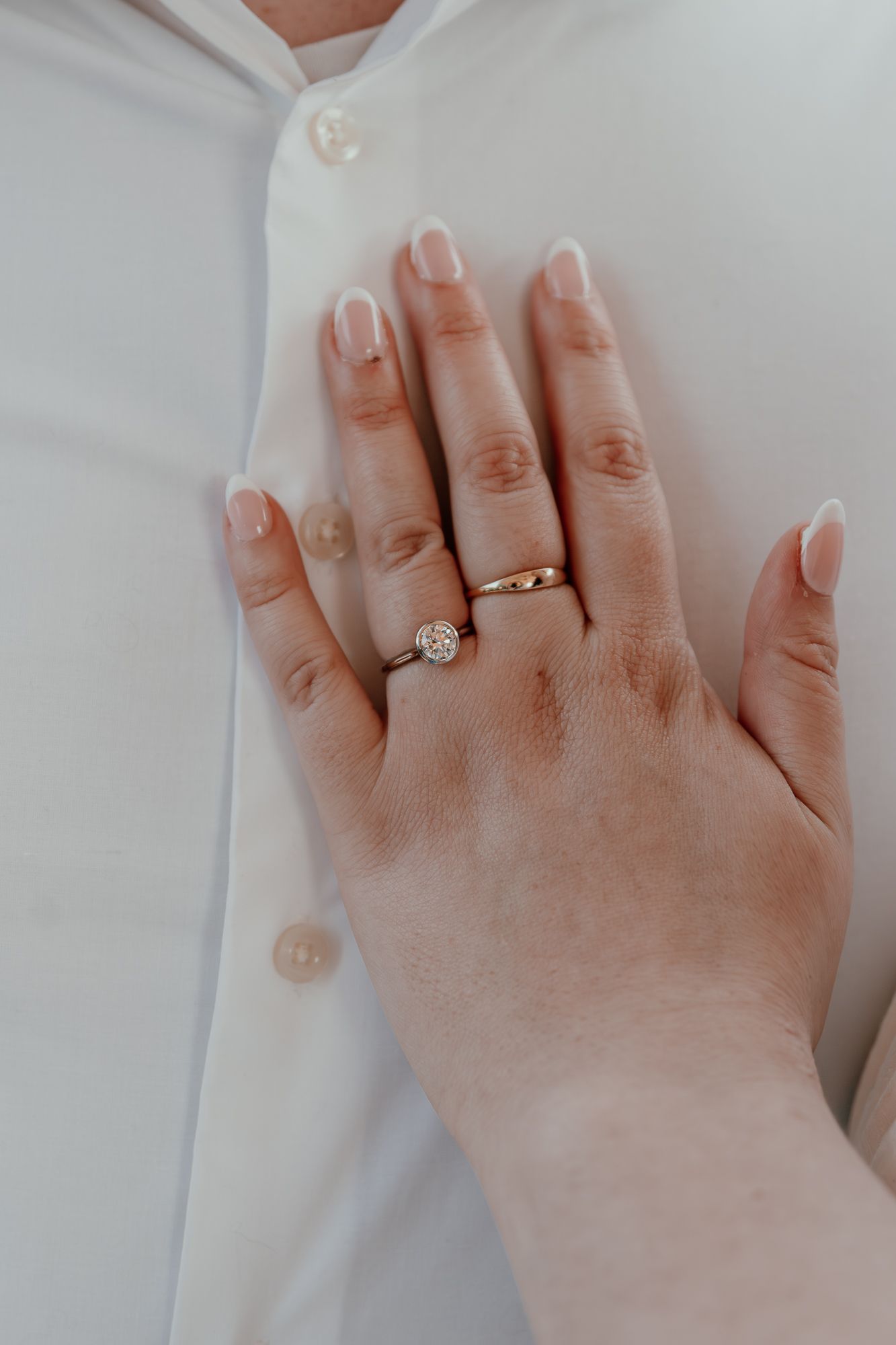 Close-up of diamond engagement ring on hand against white shirt background.