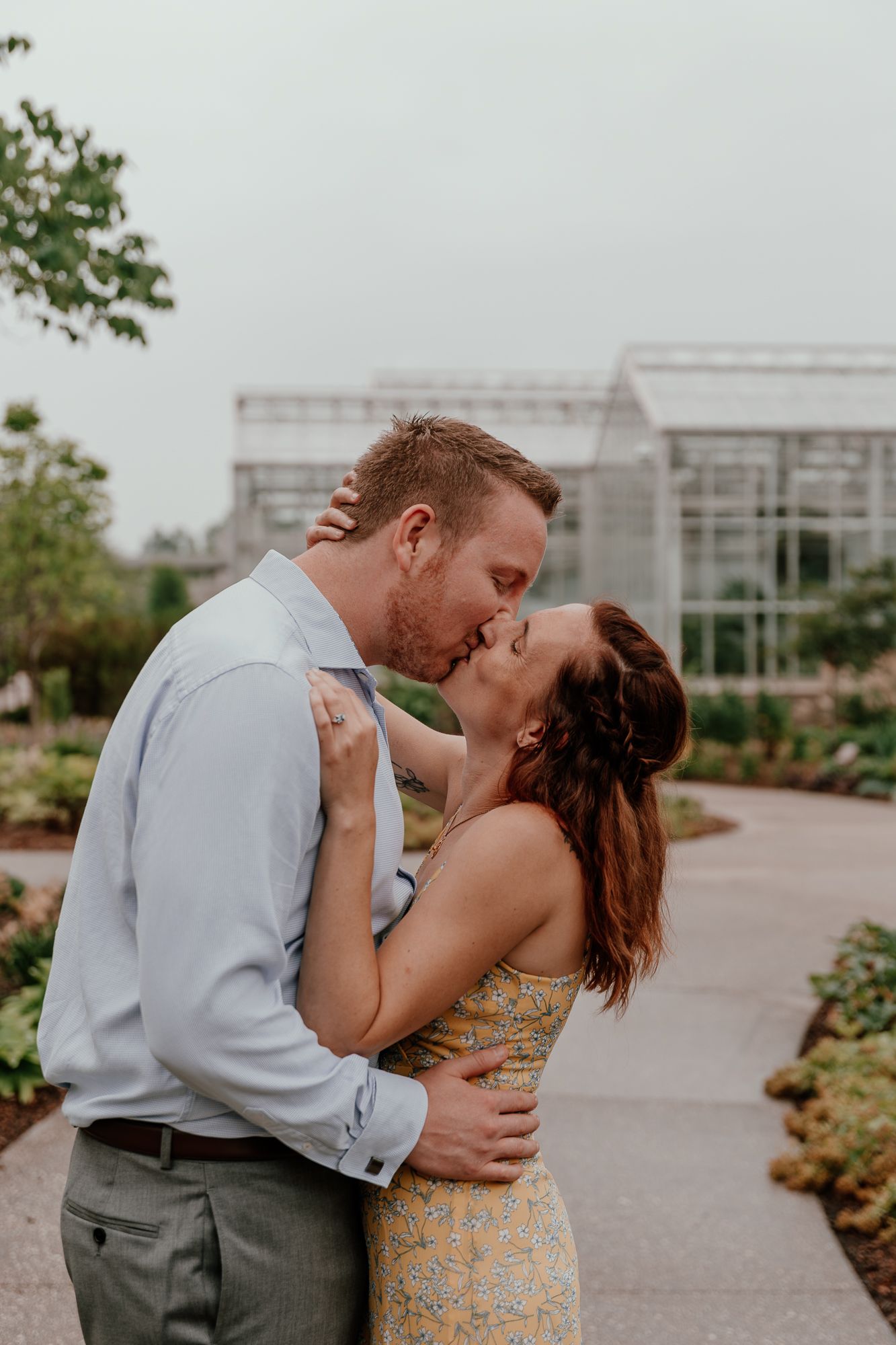 An intimate kiss shared between an engaged couple in front of a modern glass building.